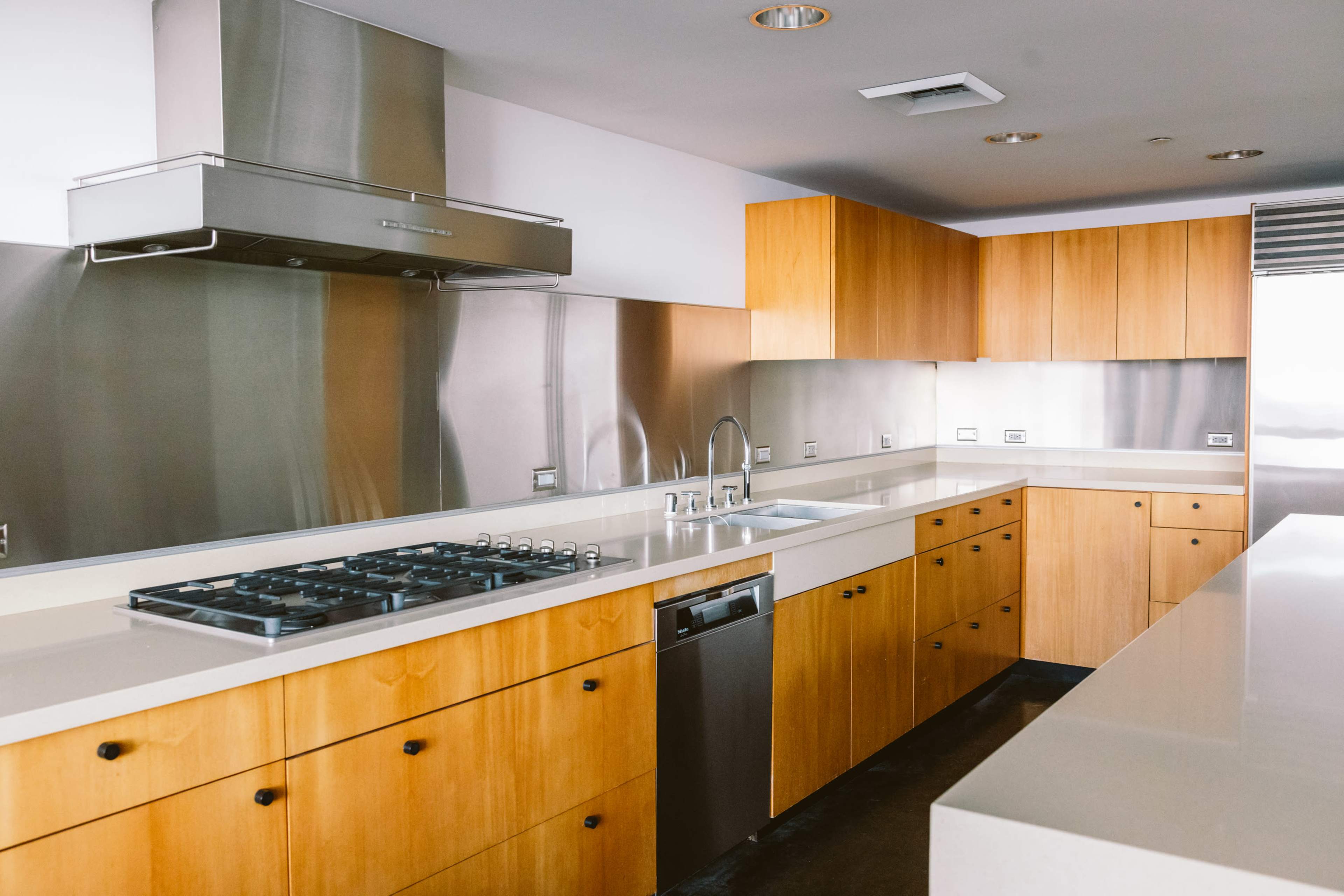 The image depicts a modern kitchen with metallic and wooden cabinetry, a gas stove, and a sleek countertop.