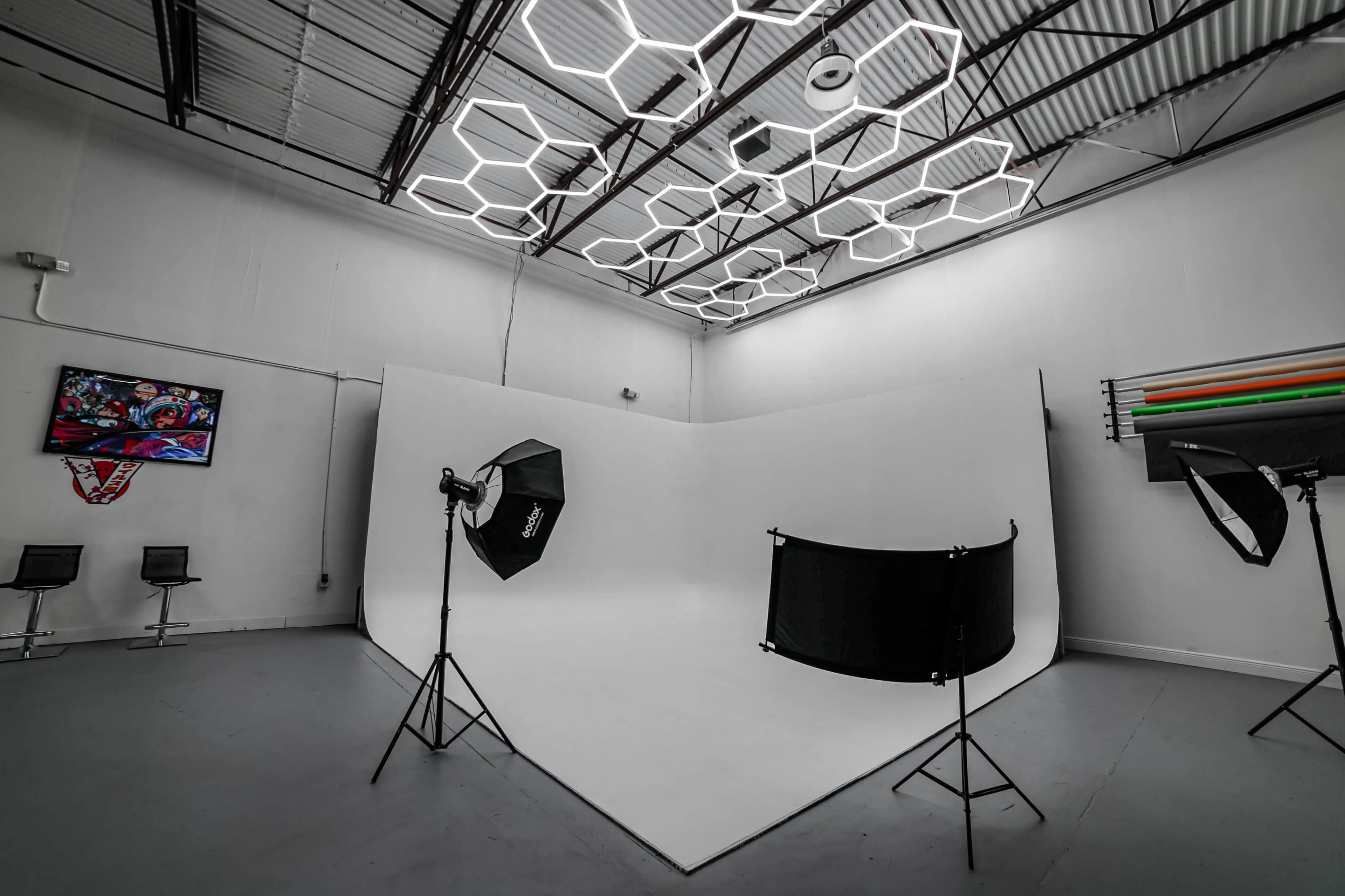 A photography studio featuring a white backdrop, lighting equipment on stands, and a hexagonal ceiling design.
