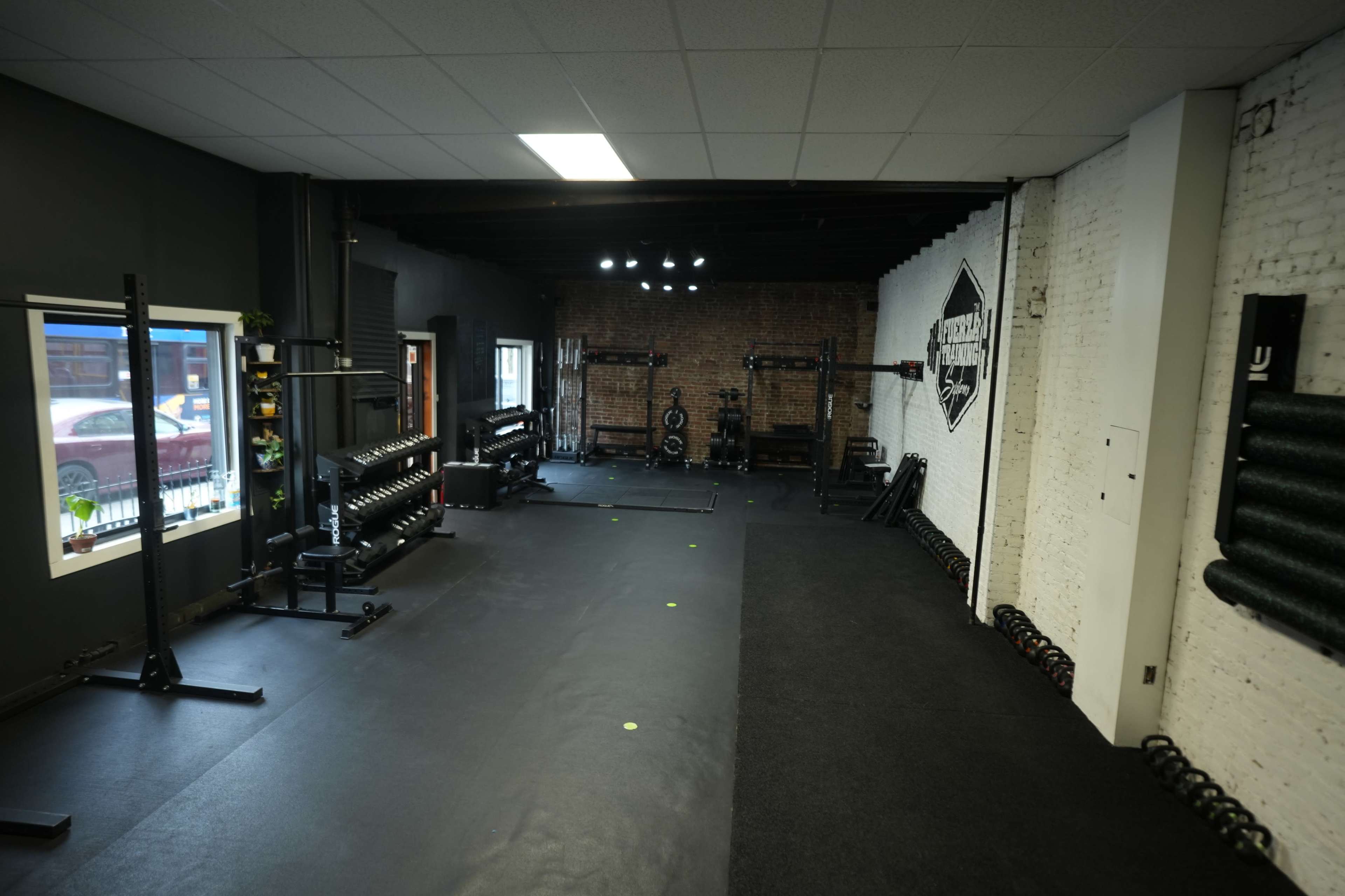 A well-equipped gym with a rubber floor, free weights, and various workout stations against exposed brick walls.
