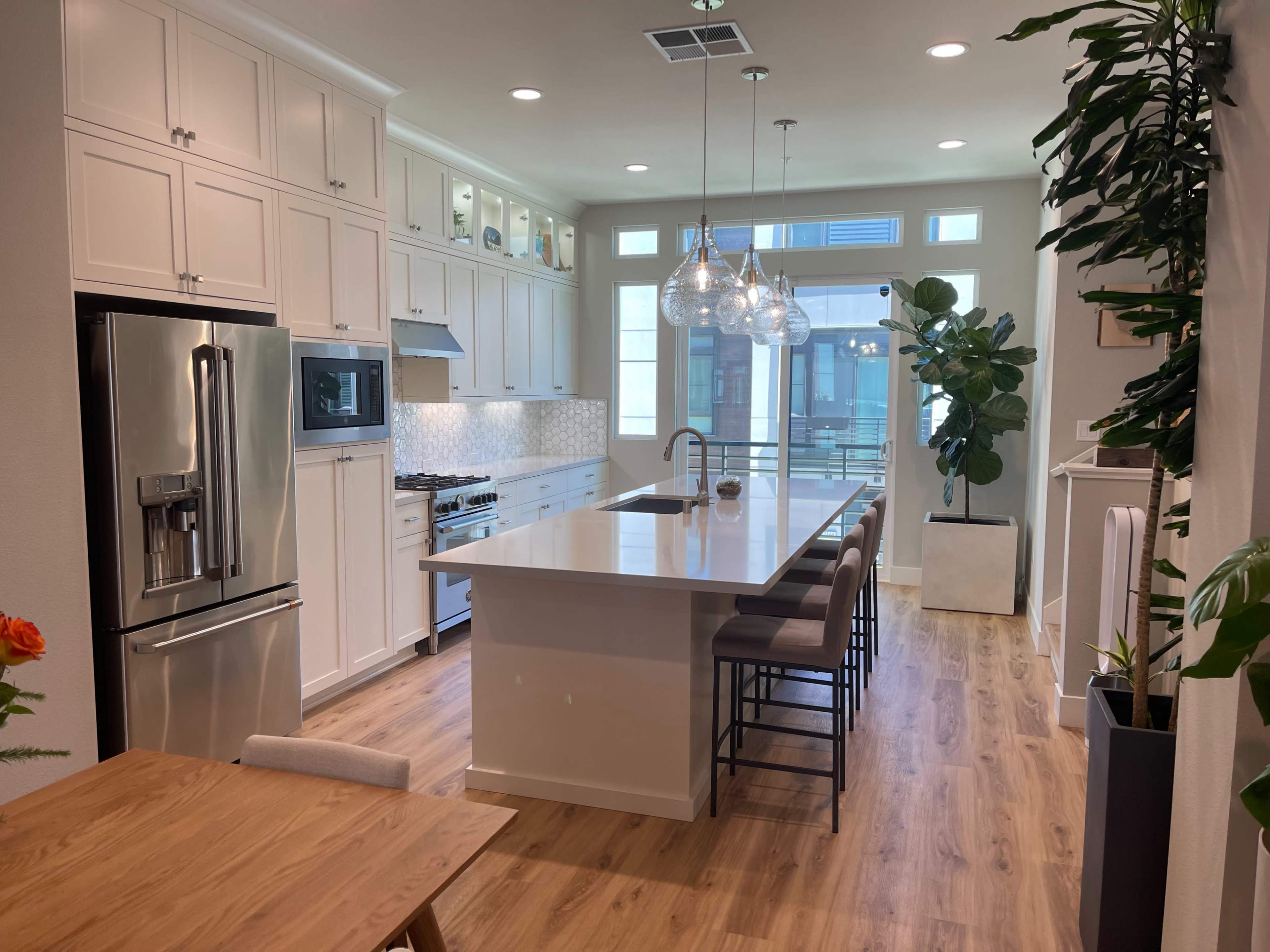 A modern kitchen with white cabinets, a large island with bar stools, and natural light streaming through large windows.