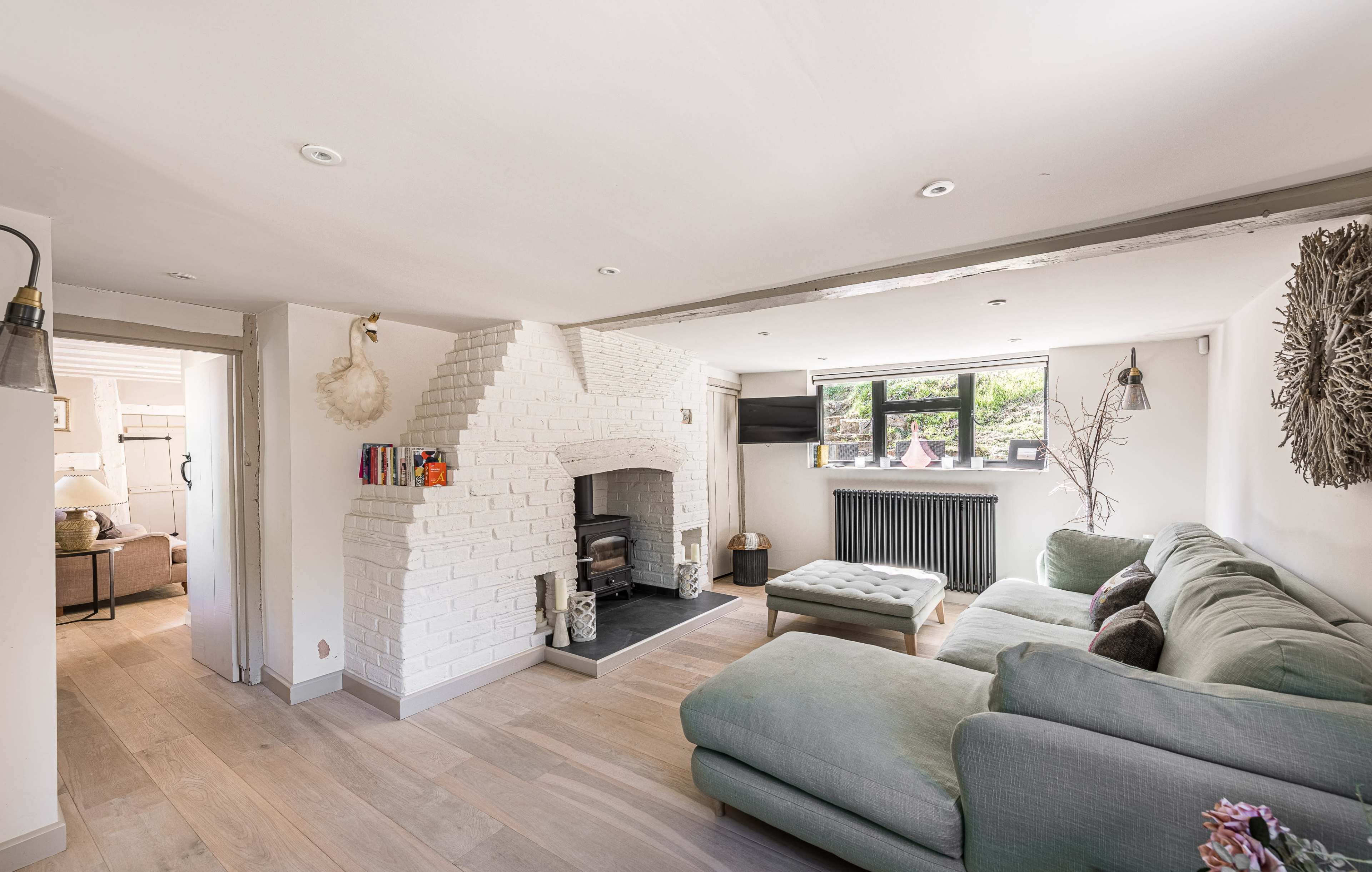 The image shows a modern living room featuring a white brick fireplace, a sectional sofa, and large windows providing natural light.