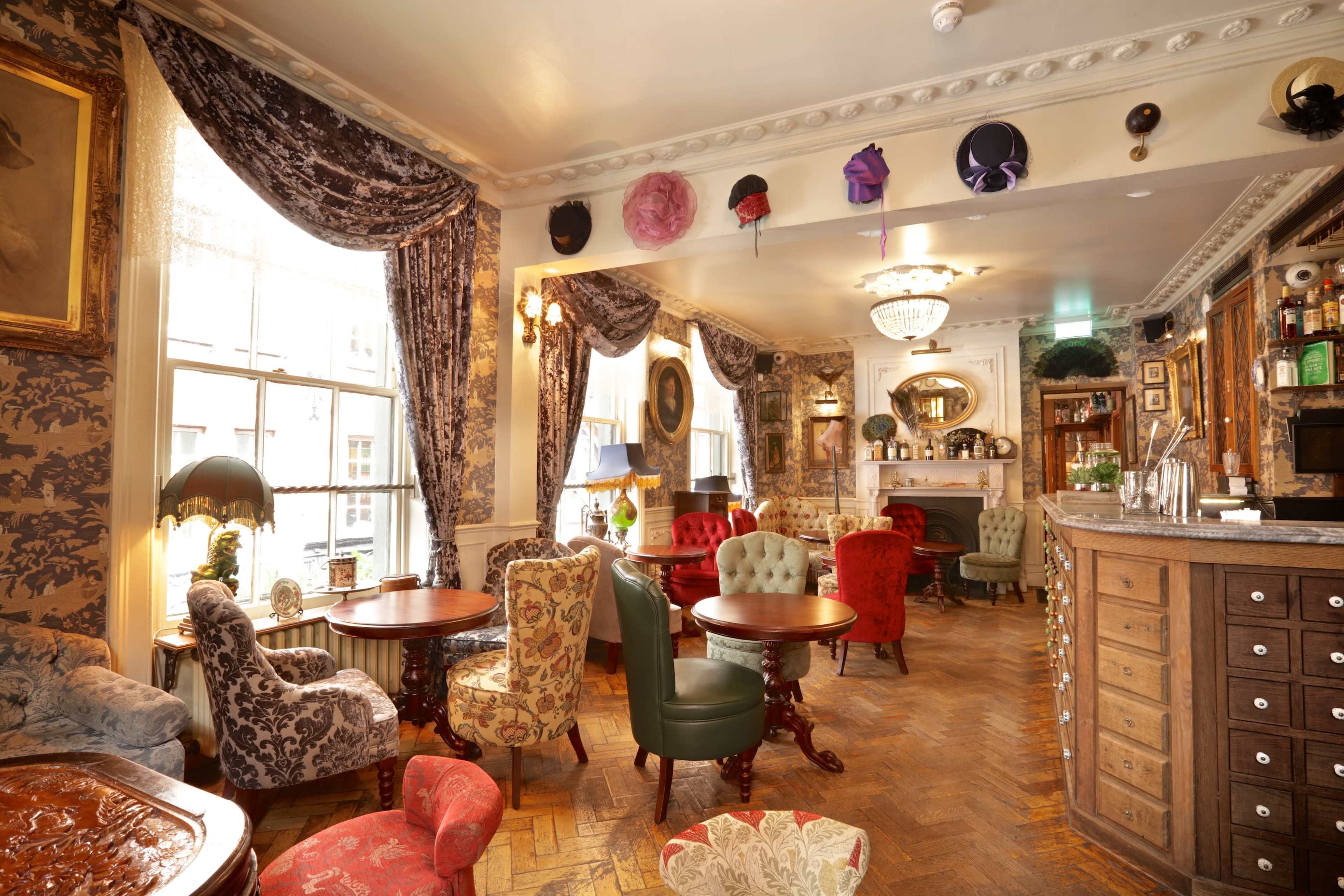 A vintage-style bar with ornate furnishings, patterned curtains, and a variety of seating arrangements in a well-lit room.
