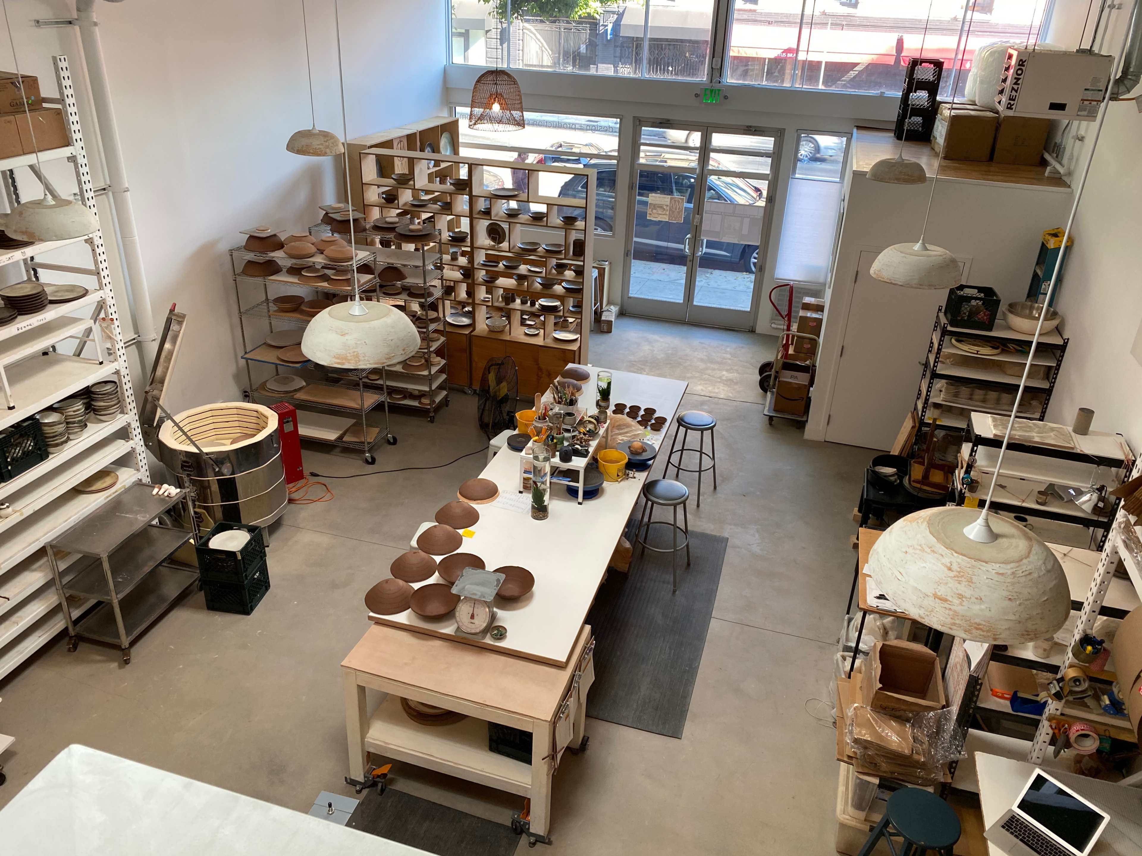 A spacious pottery studio features a central work table surrounded by shelves of completed ceramic pieces and equipment.