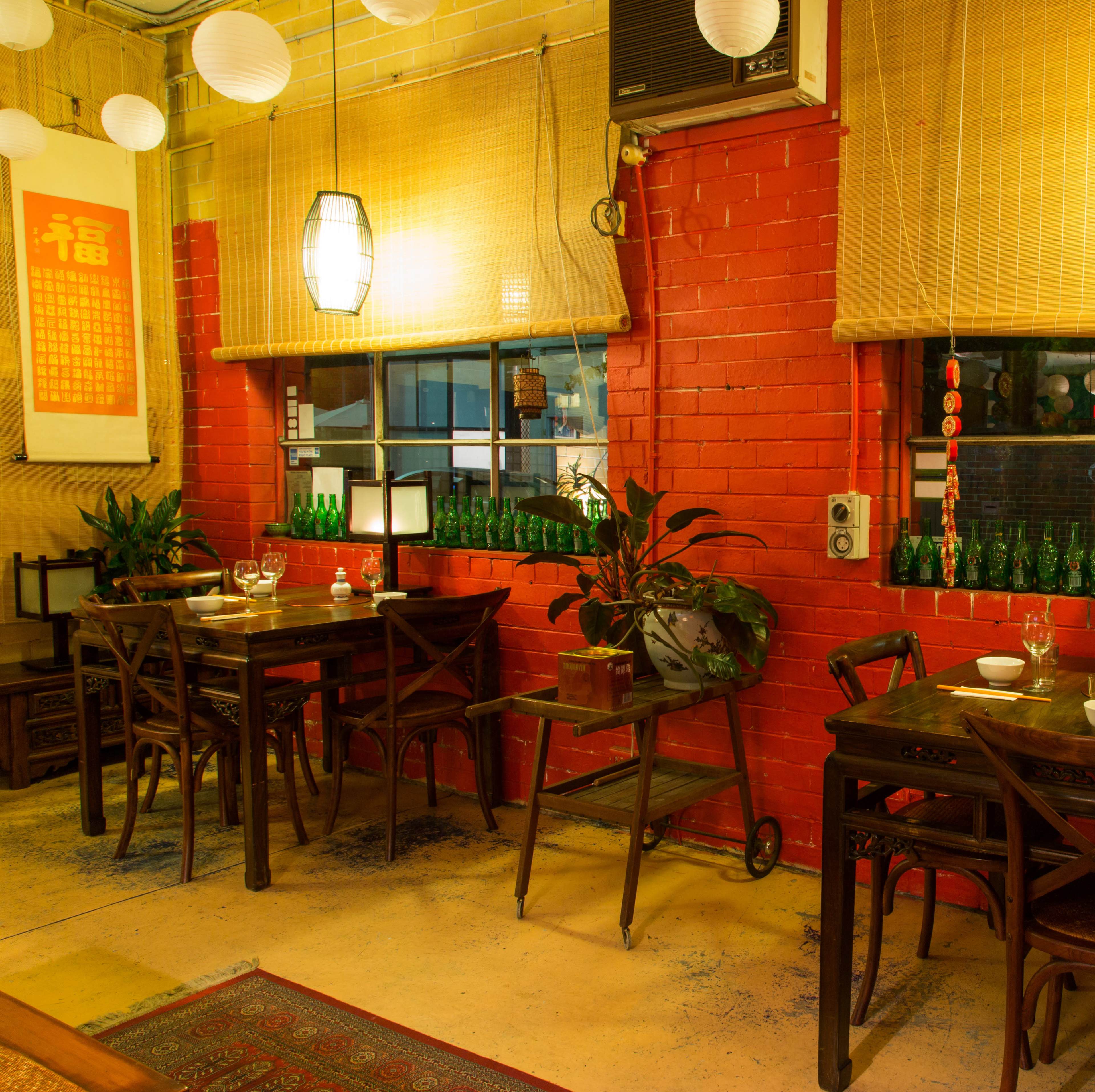 A cozy restaurant interior with wooden tables and chairs, green glass bottles on the windowsill, and decorative lanterns hanging from the ceiling.