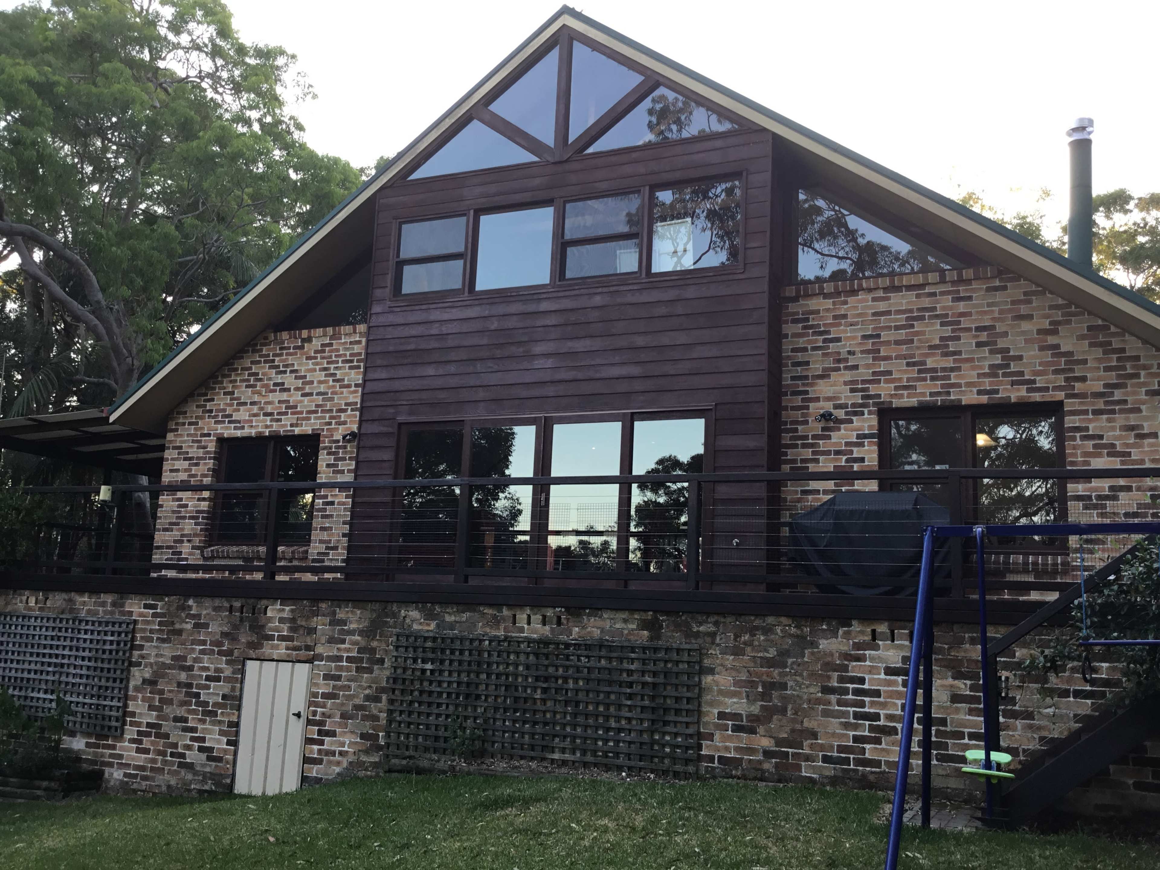 A two-story house with a combination of brick and wooden siding, featuring large windows and a balcony that overlooks a grassy yard.