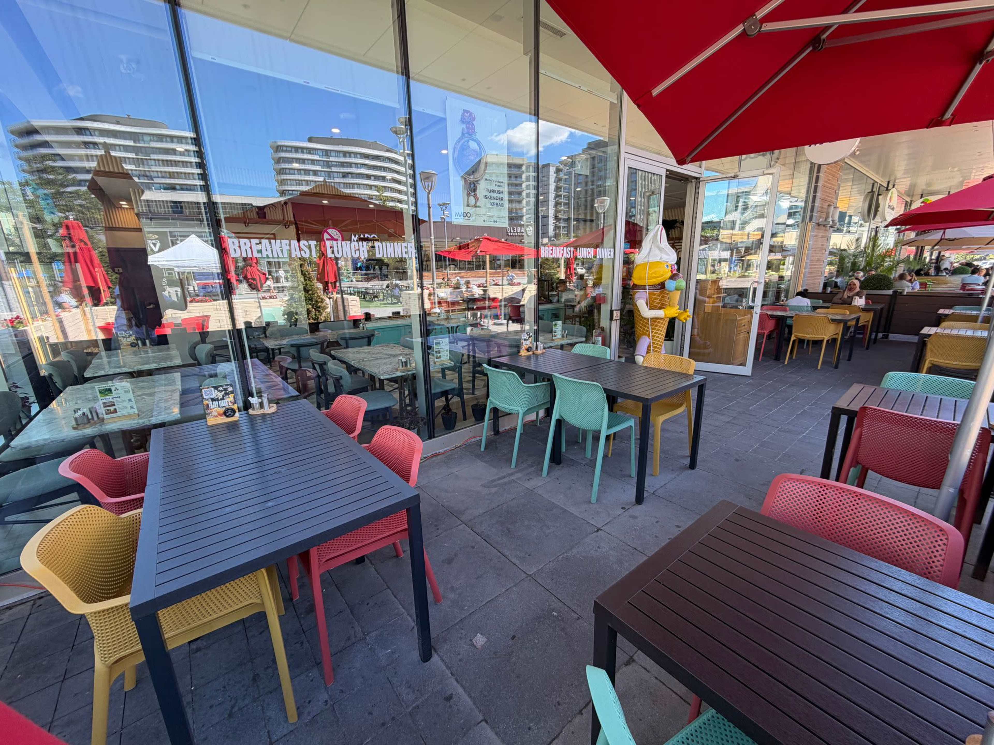 The image shows an outdoor dining area of a restaurant with colorful chairs and tables, along with large umbrellas providing shade.