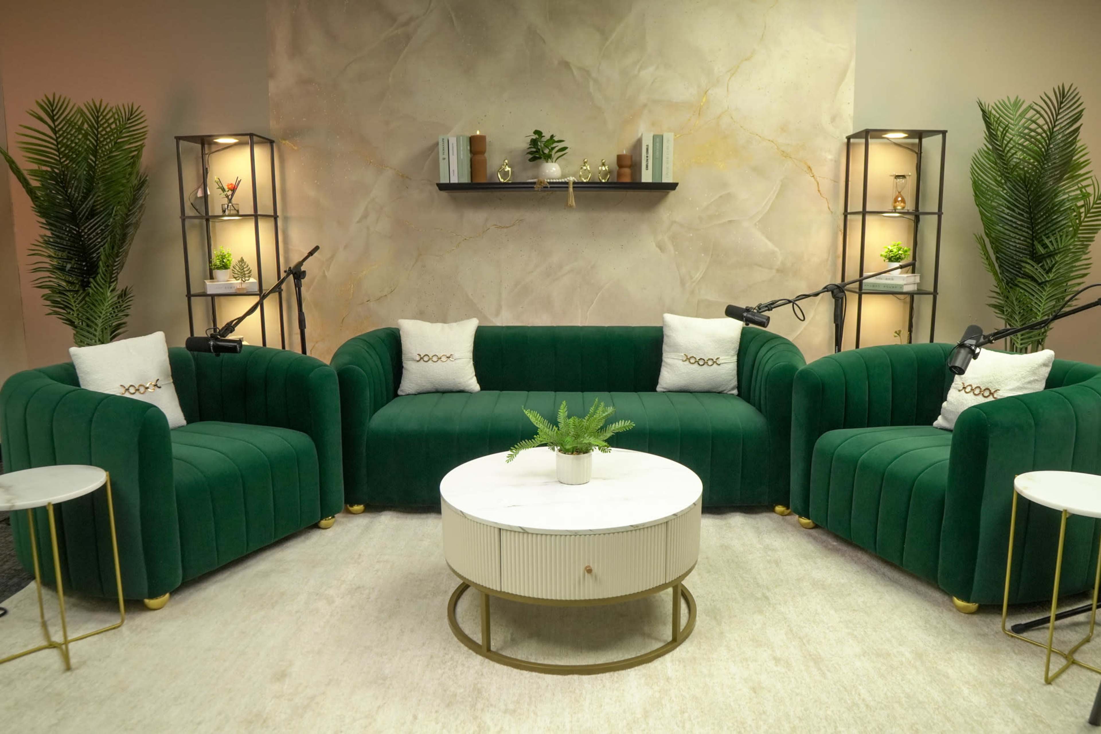 The image features a modern, green velvet seating area with two sofas and a circular coffee table, surrounded by decorative plants and shelving units.