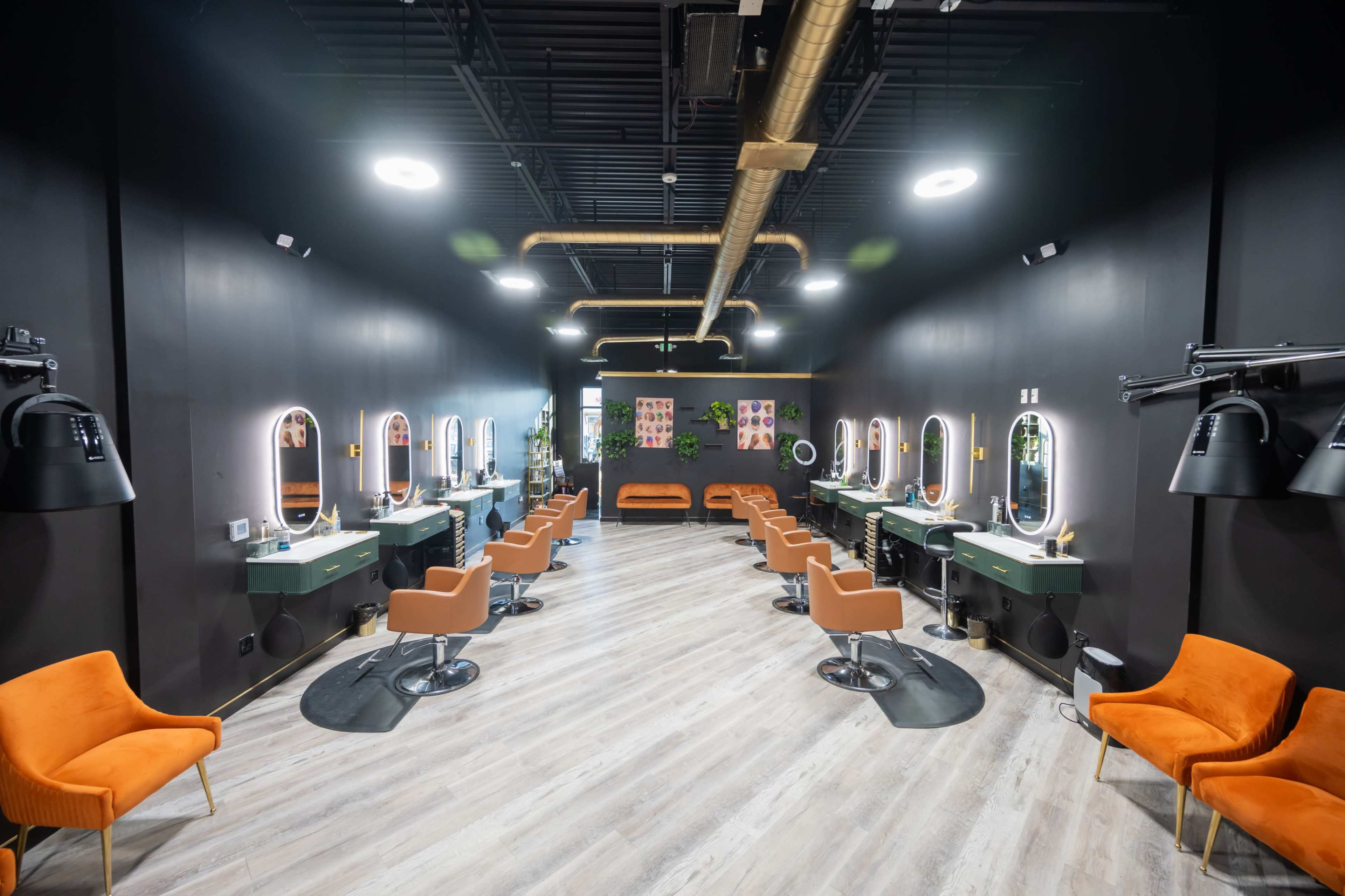 The image shows a modern hair salon with multiple styling stations, each featuring round mirrors and orange chairs, all arranged in a spacious, dimly lit room.