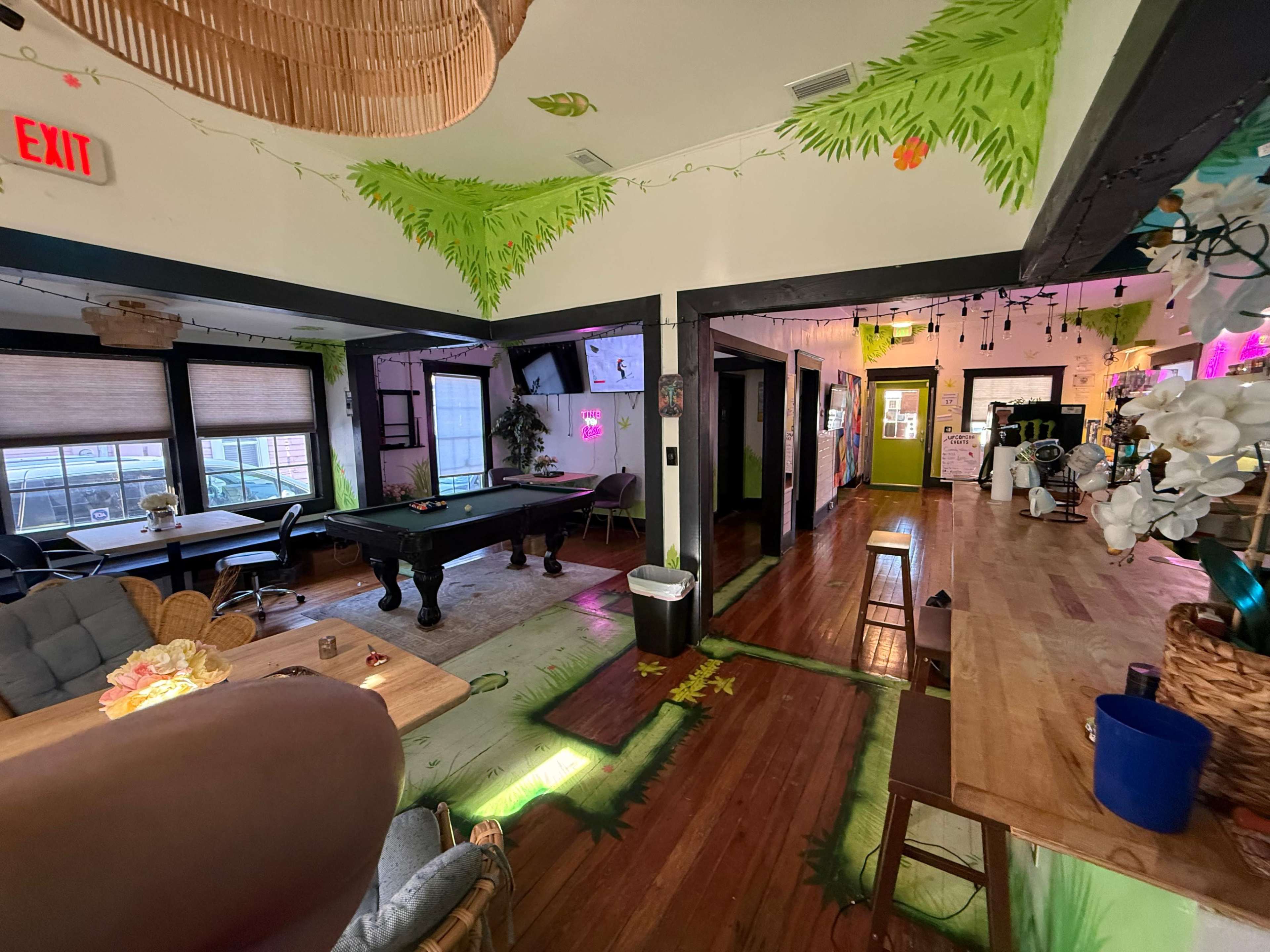 The interior of a vibrant social space features a pool table, various seating areas, and colorful decorations on the walls and ceiling.