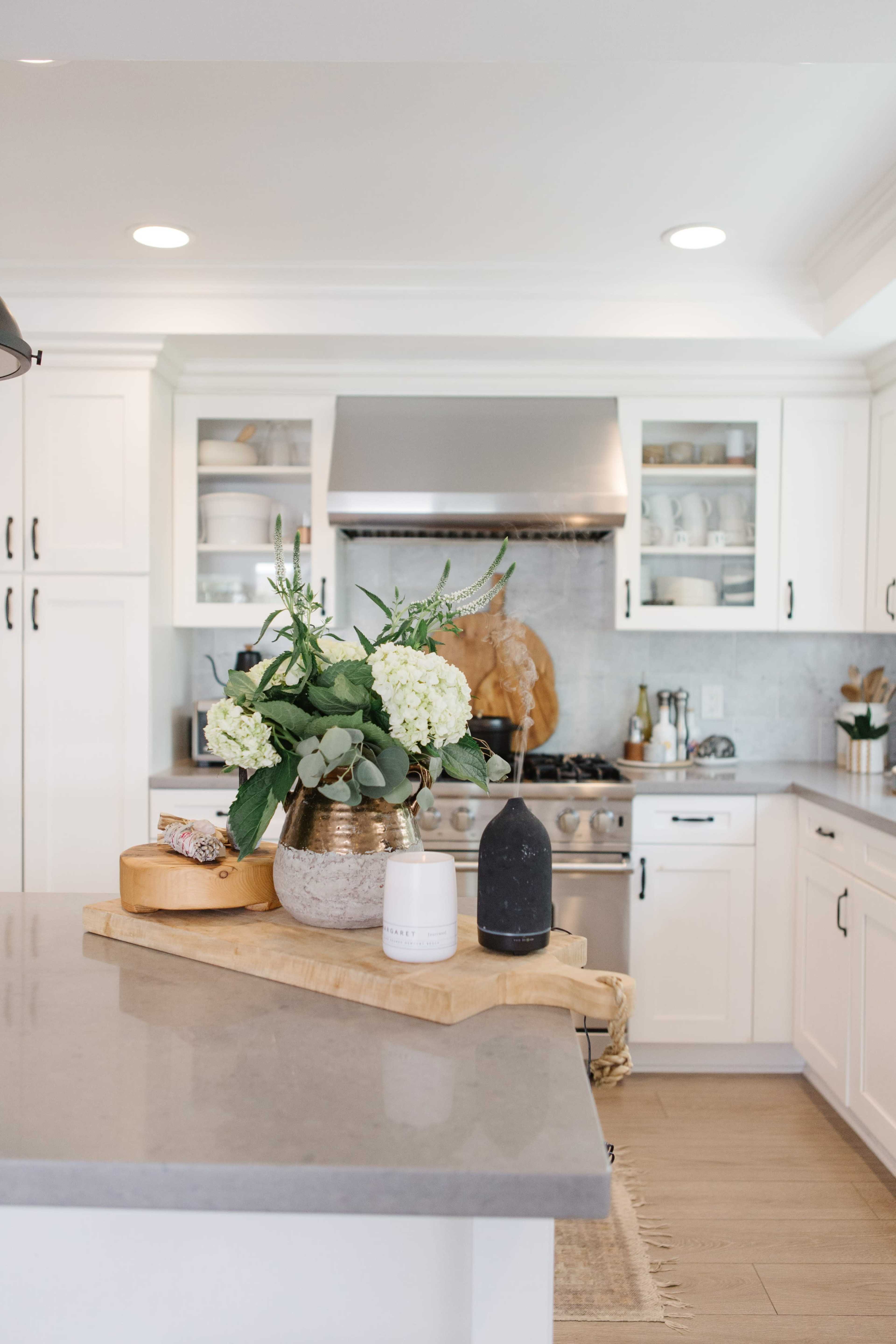A modern kitchen features a stove, white cabinetry, and a countertop with a floral arrangement and wooden cutting board.