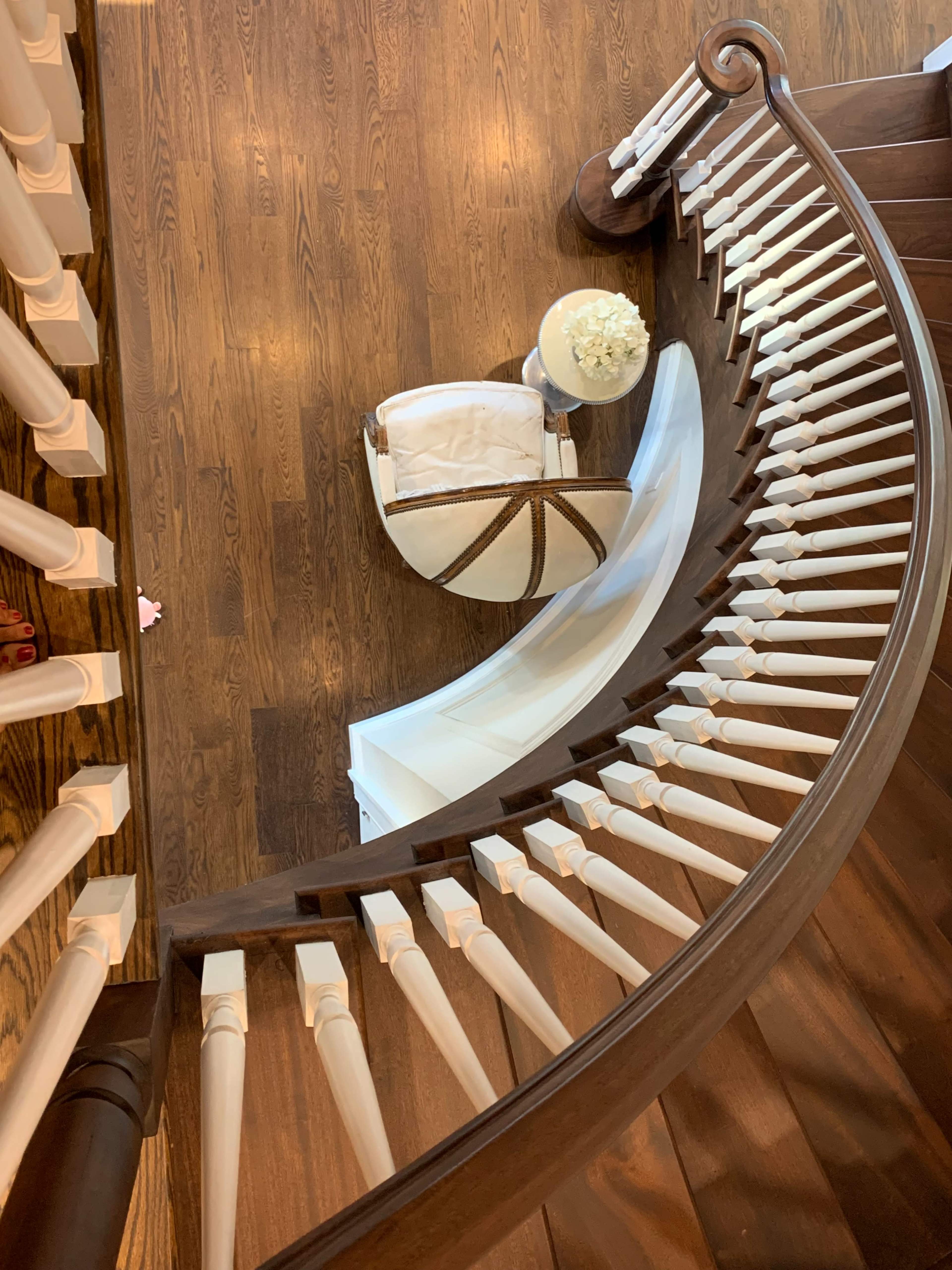 A curved wooden staircase with white banisters, leading down to a small seating area adorned with a table and a floral arrangement.