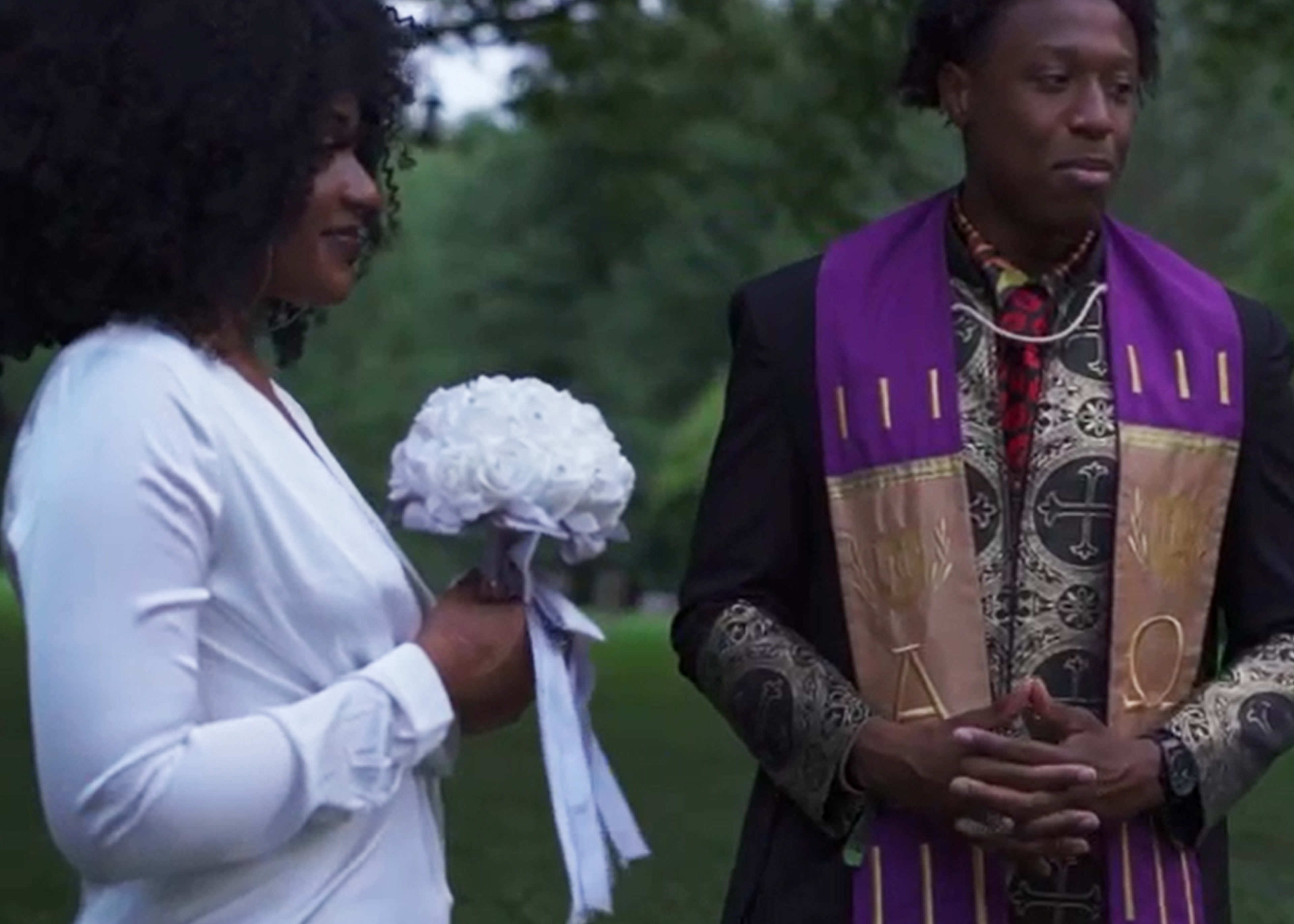 A woman in a white dress holds a bouquet while standing next to a man in traditional ceremonial attire.