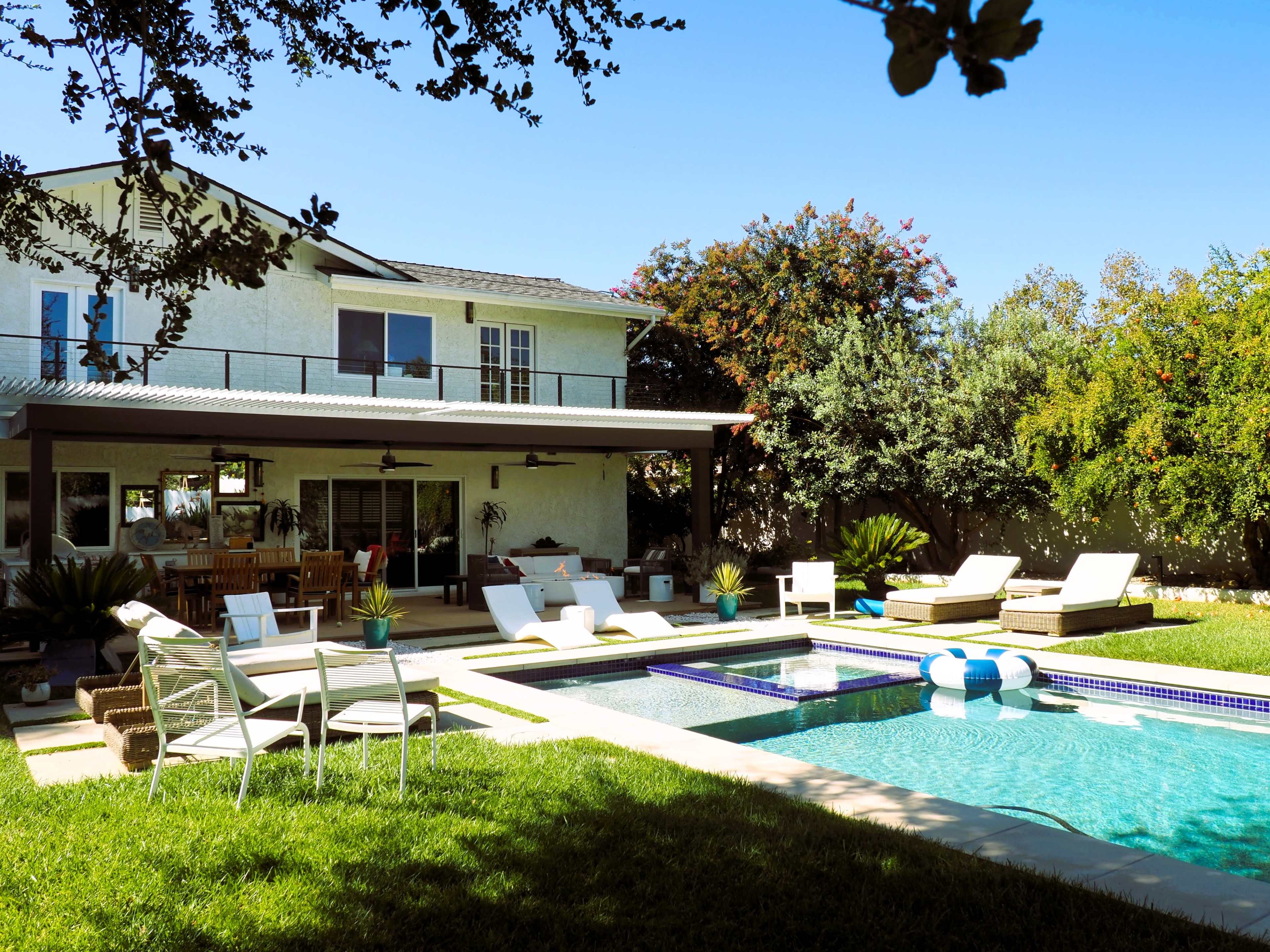A spacious backyard features a swimming pool, sun loungers, and a two-story house with a covered patio.
