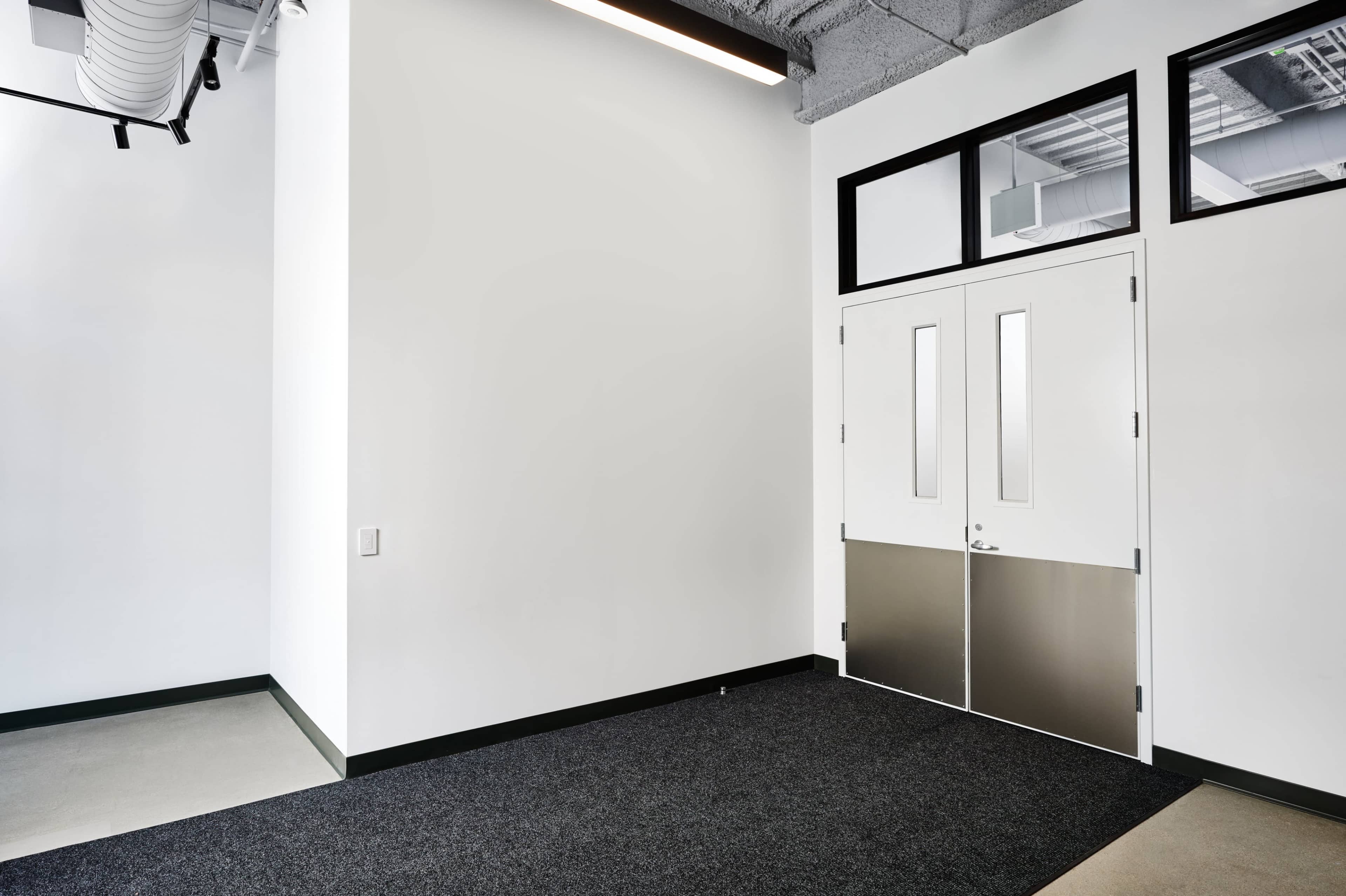 A bright, minimalistic entrance with double doors and a gray carpet leading into a room with white walls.