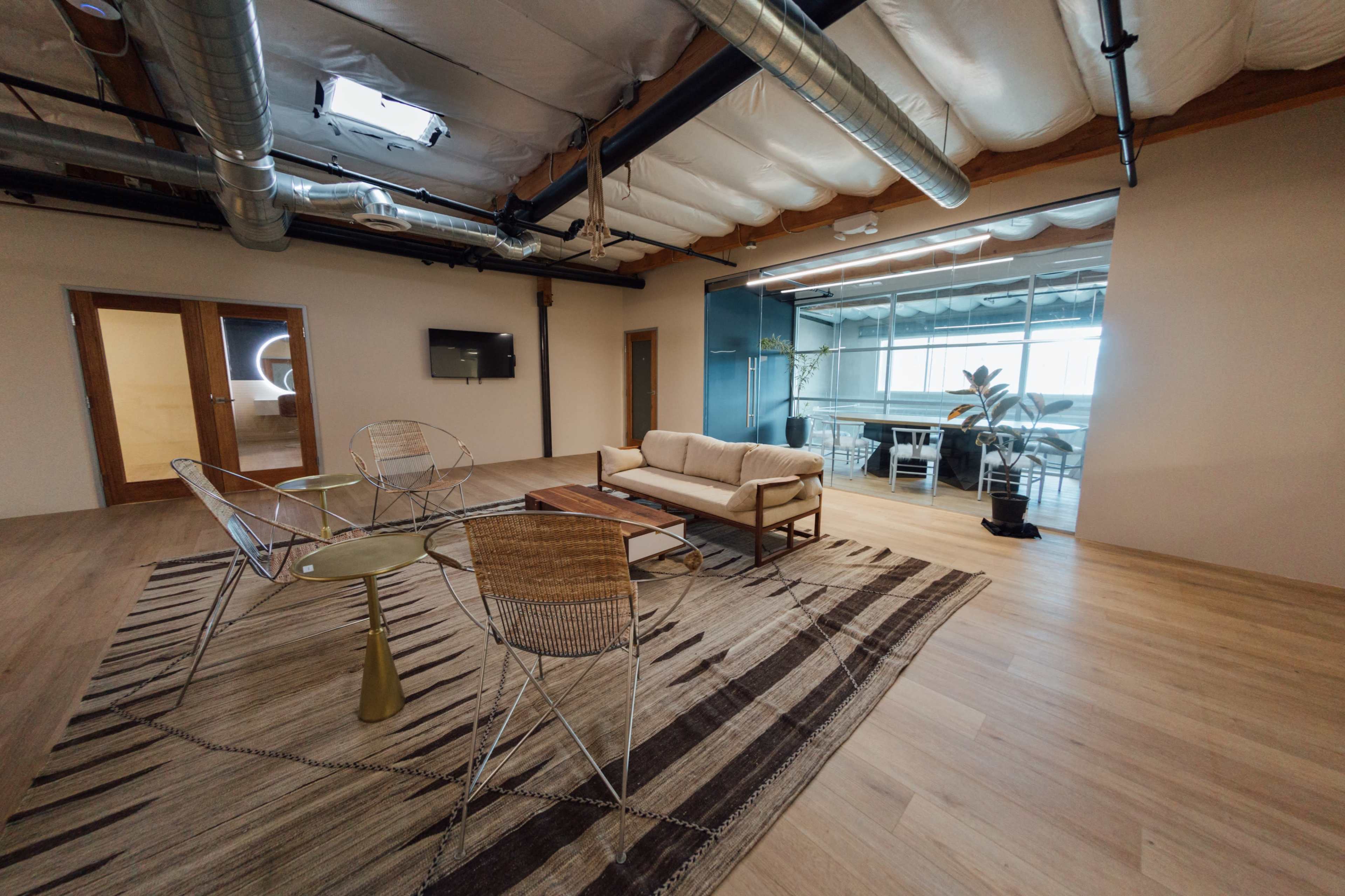 A modern office interior featuring a seating area with a couch and chairs, a coffee table, and glass-walled meeting rooms in the background.