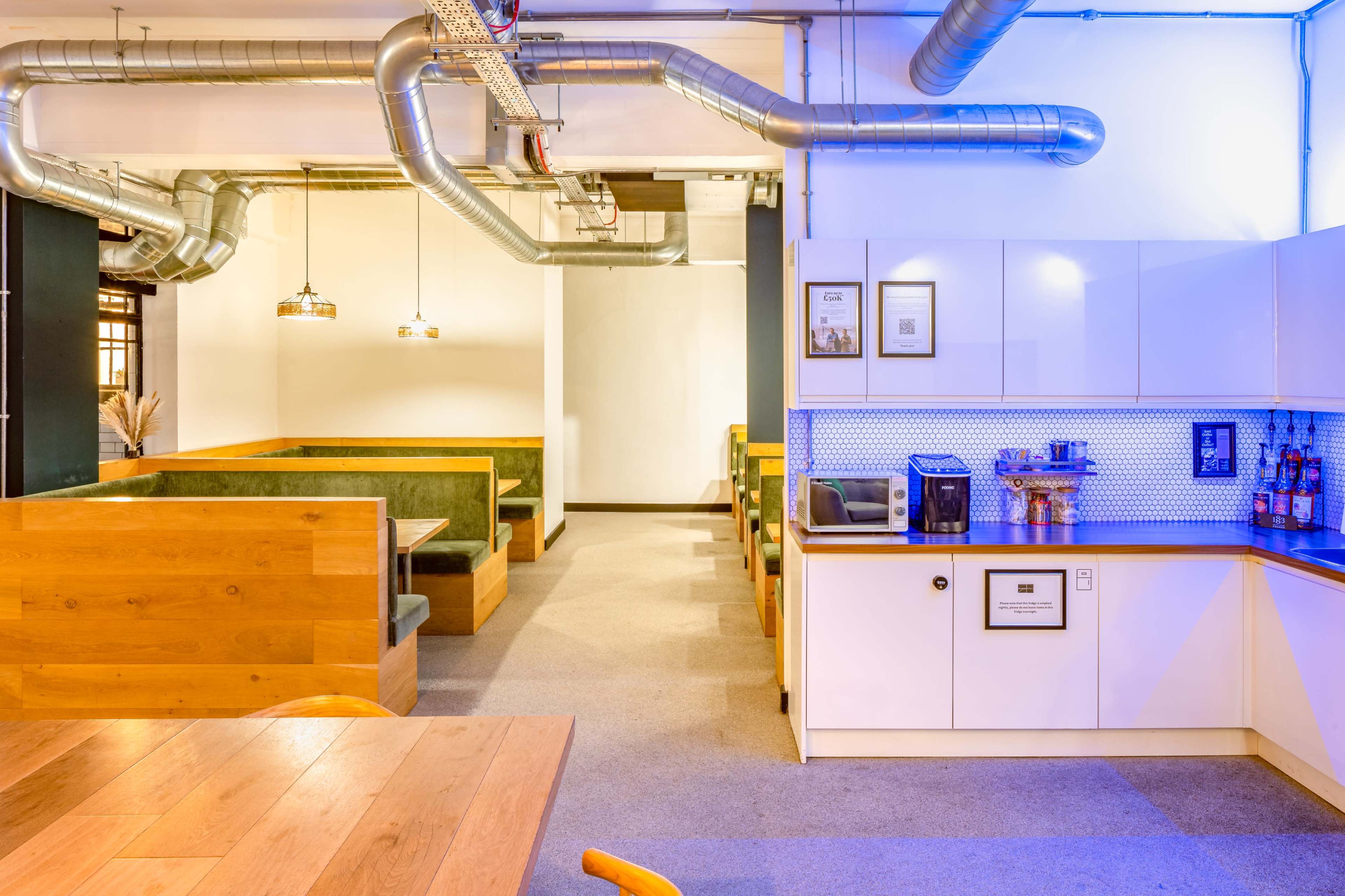 A modern café interior with wooden seating, a kitchenette area, and visible ductwork along the ceiling.