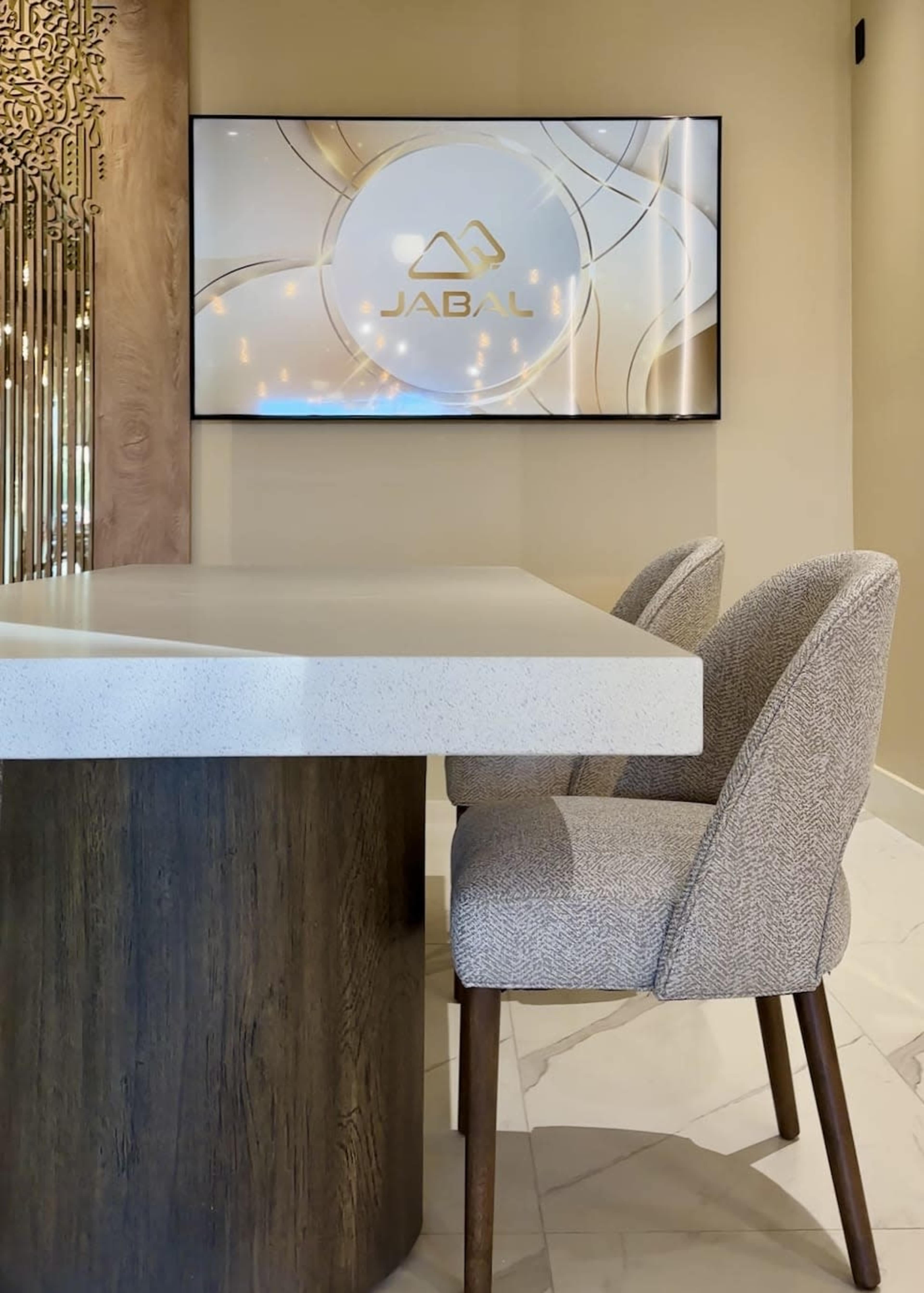 A modern interior space features a sleek table, stylish chair, and a wall-mounted television displaying the "JABAL" logo.