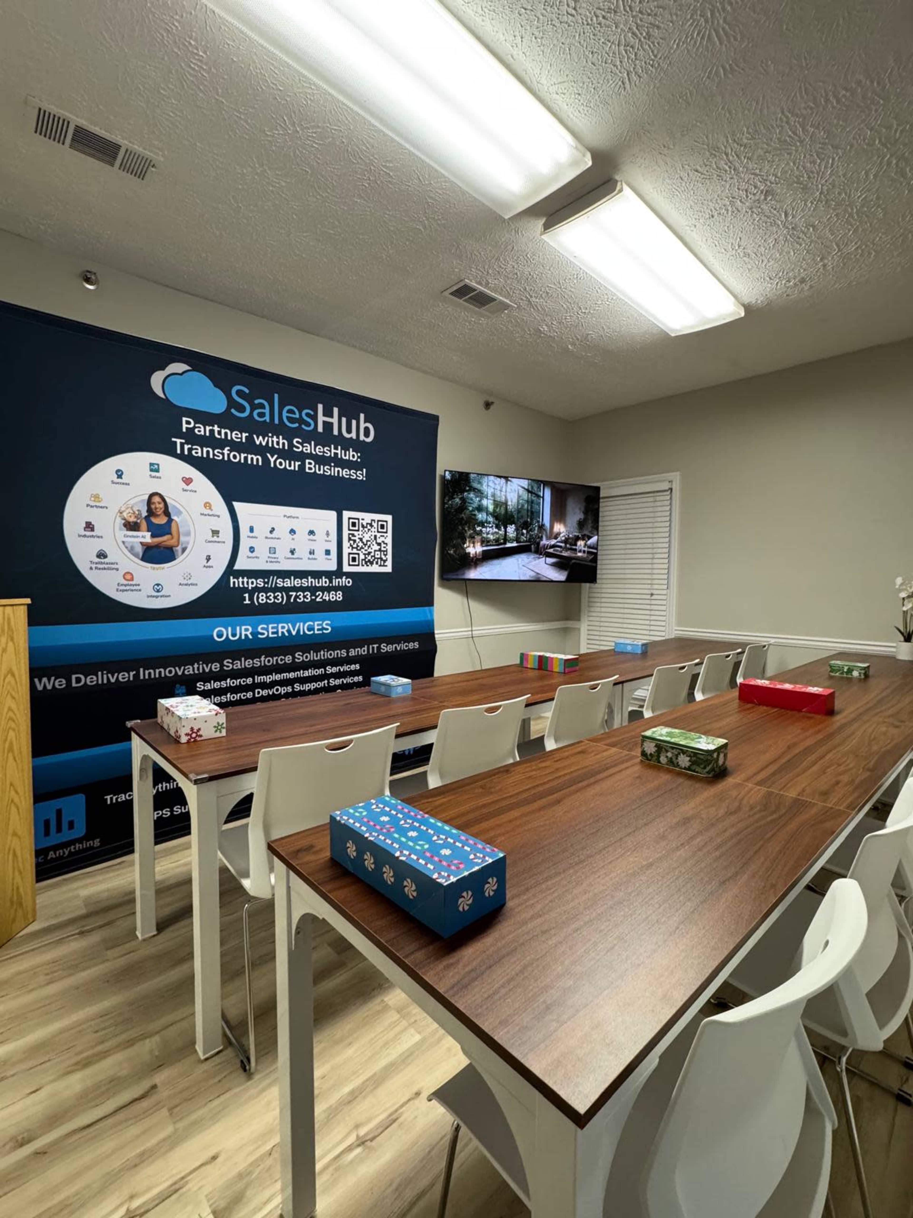 A conference room features a long table set with colorful gift boxes, a large wall display with branding for SalesHub, and a monitor showing visuals.