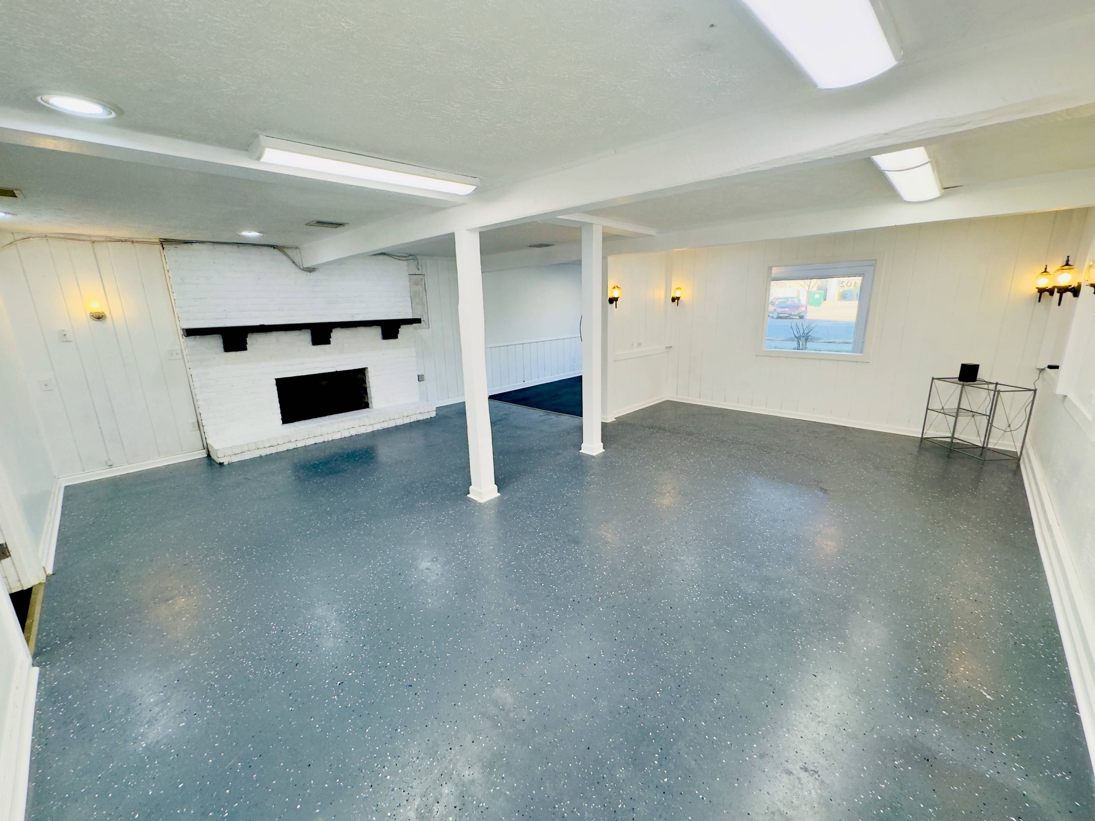 A spacious room with a white brick fireplace, light-colored walls, and a gray speckled floor.
