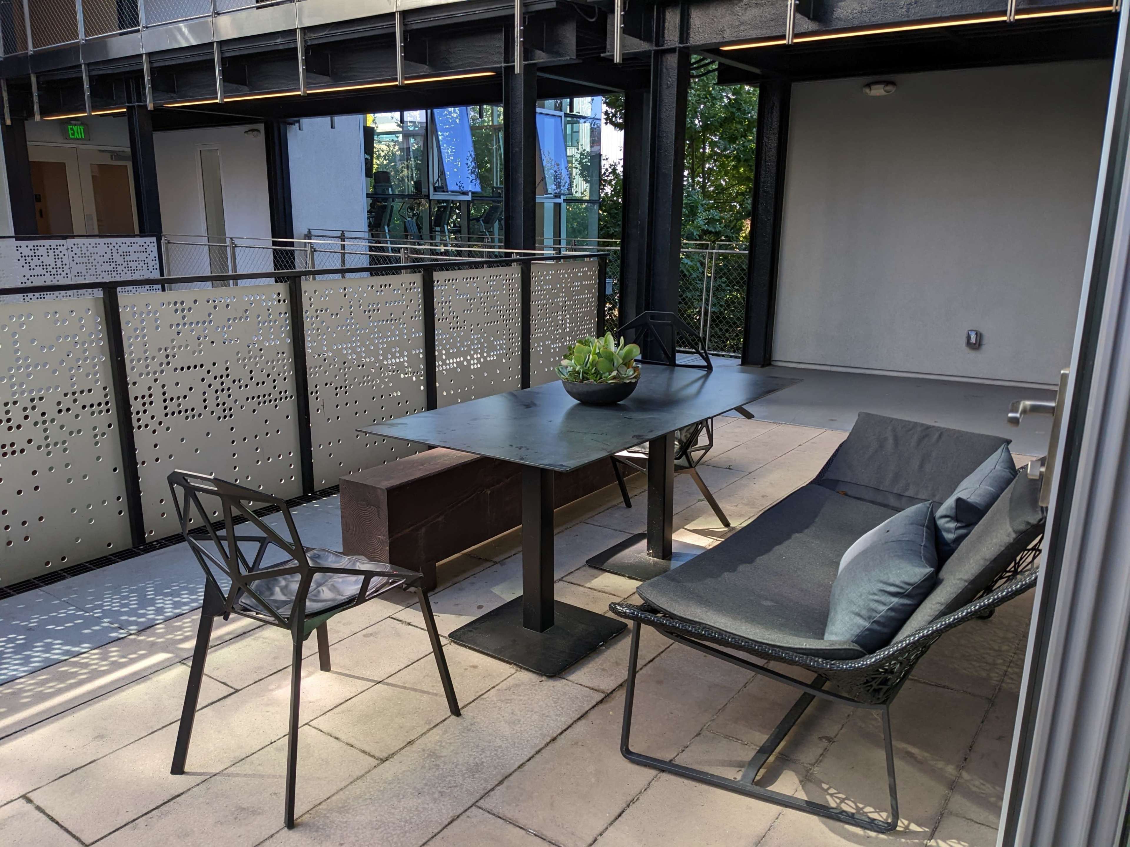 A modern outdoor space features a table with a plant centerpiece and seating options on a paved surface.