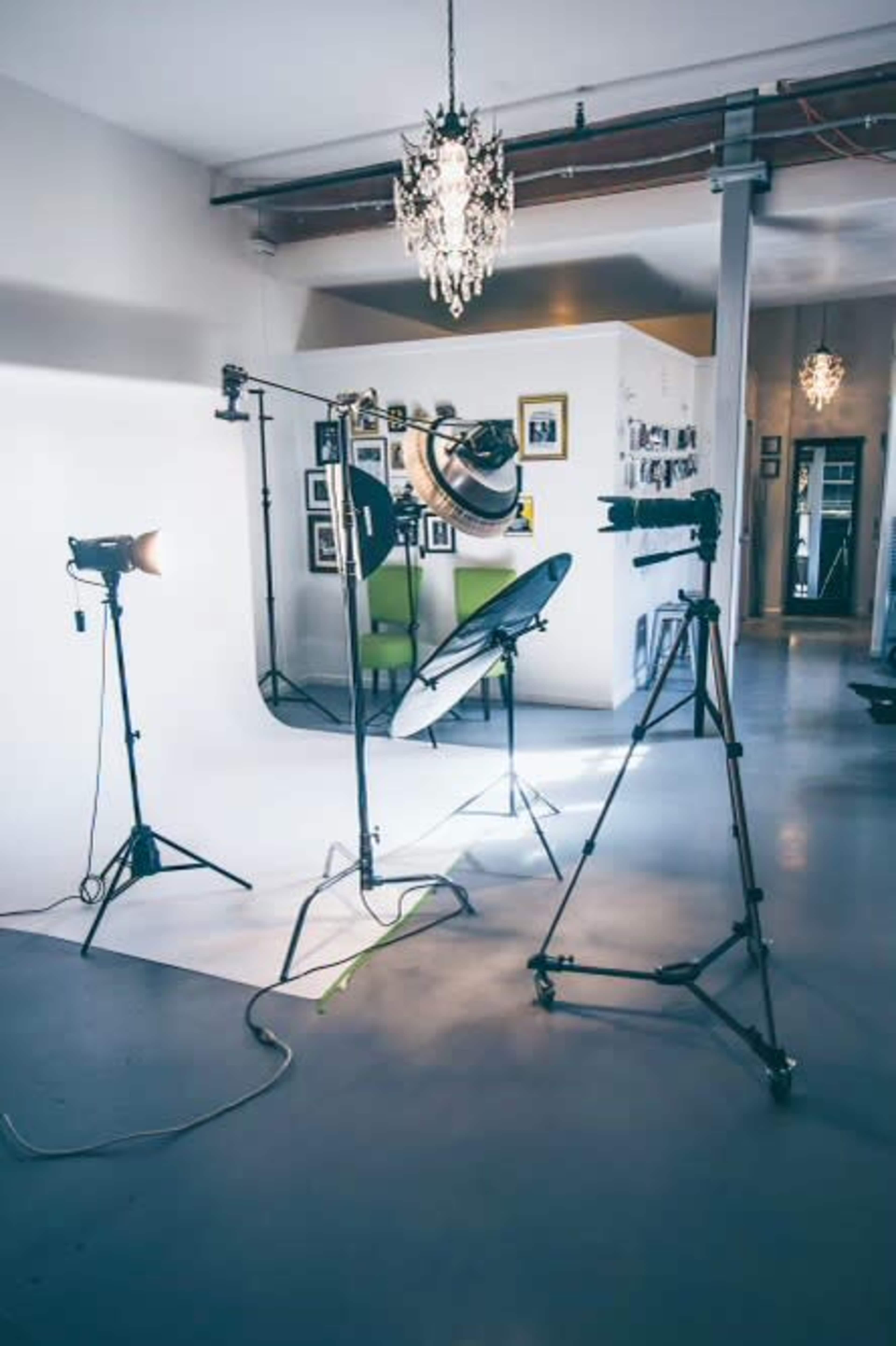 The image displays a photography studio setup with lighting equipment, a backdrop, and a camera on tripods.