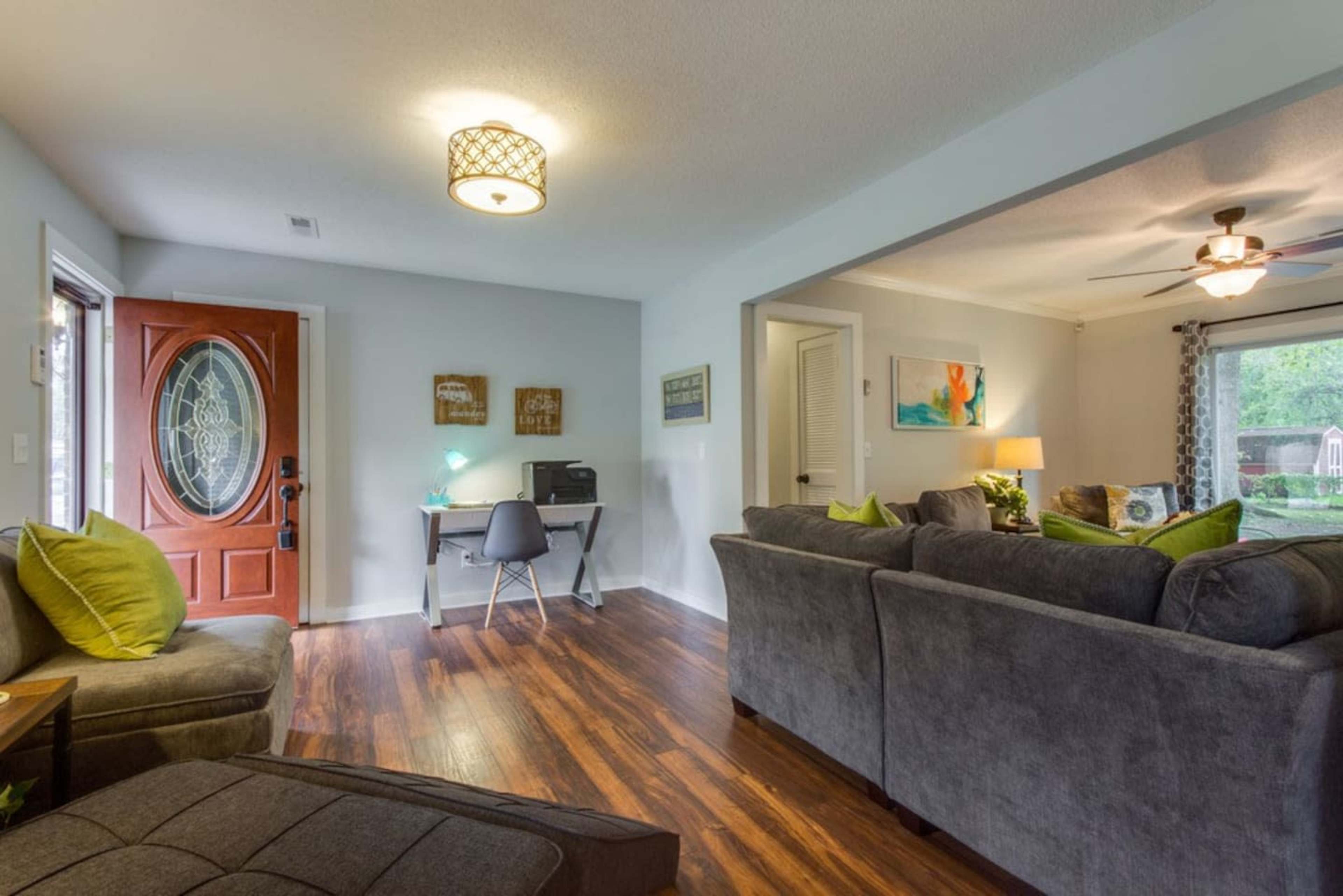 A cozy living room features a sofa, a small work desk, and a front door leading to an outdoor area.