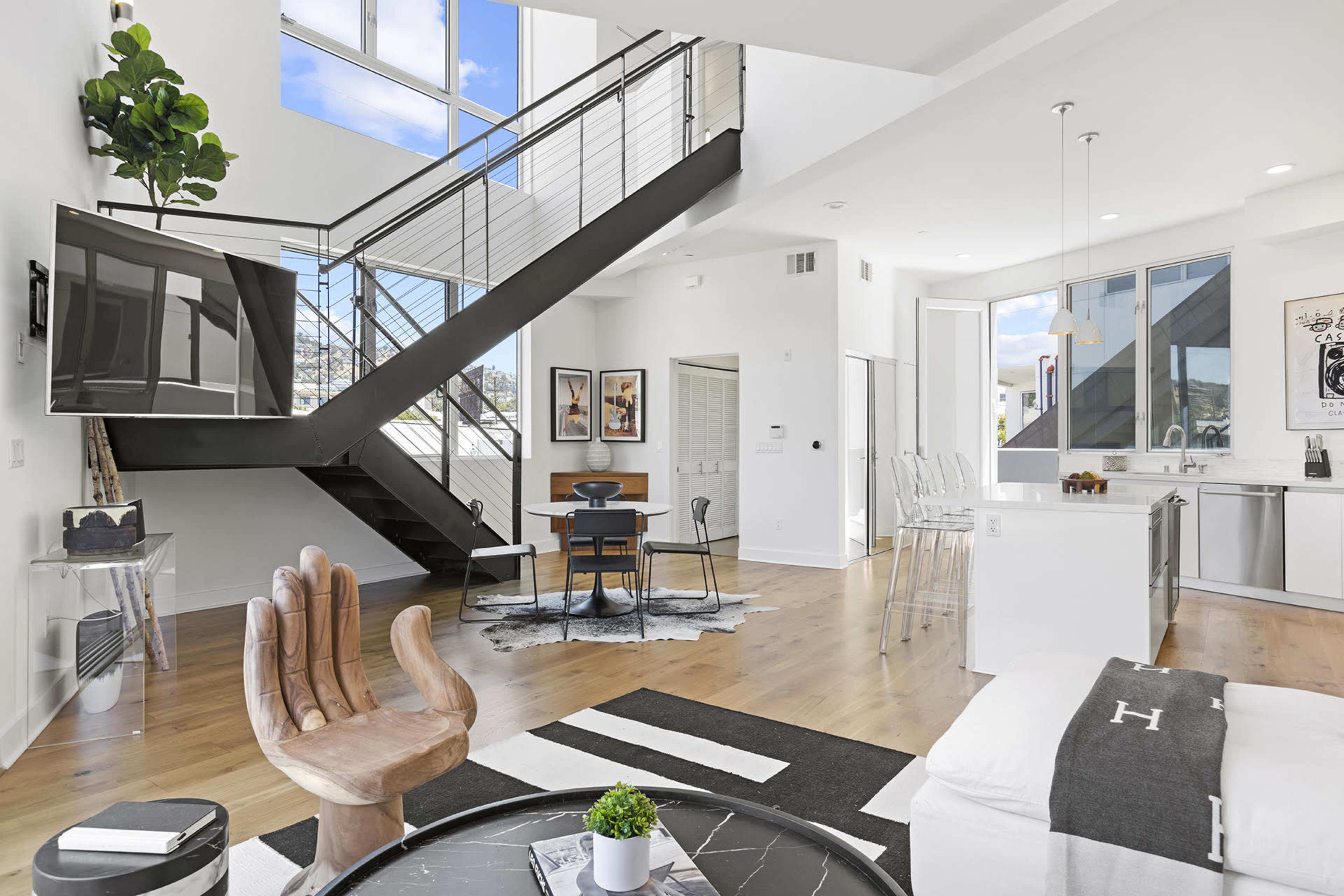 A modern, open-concept living space with a sleek staircase, a dining area, and a kitchen featuring minimalist designs and large windows.