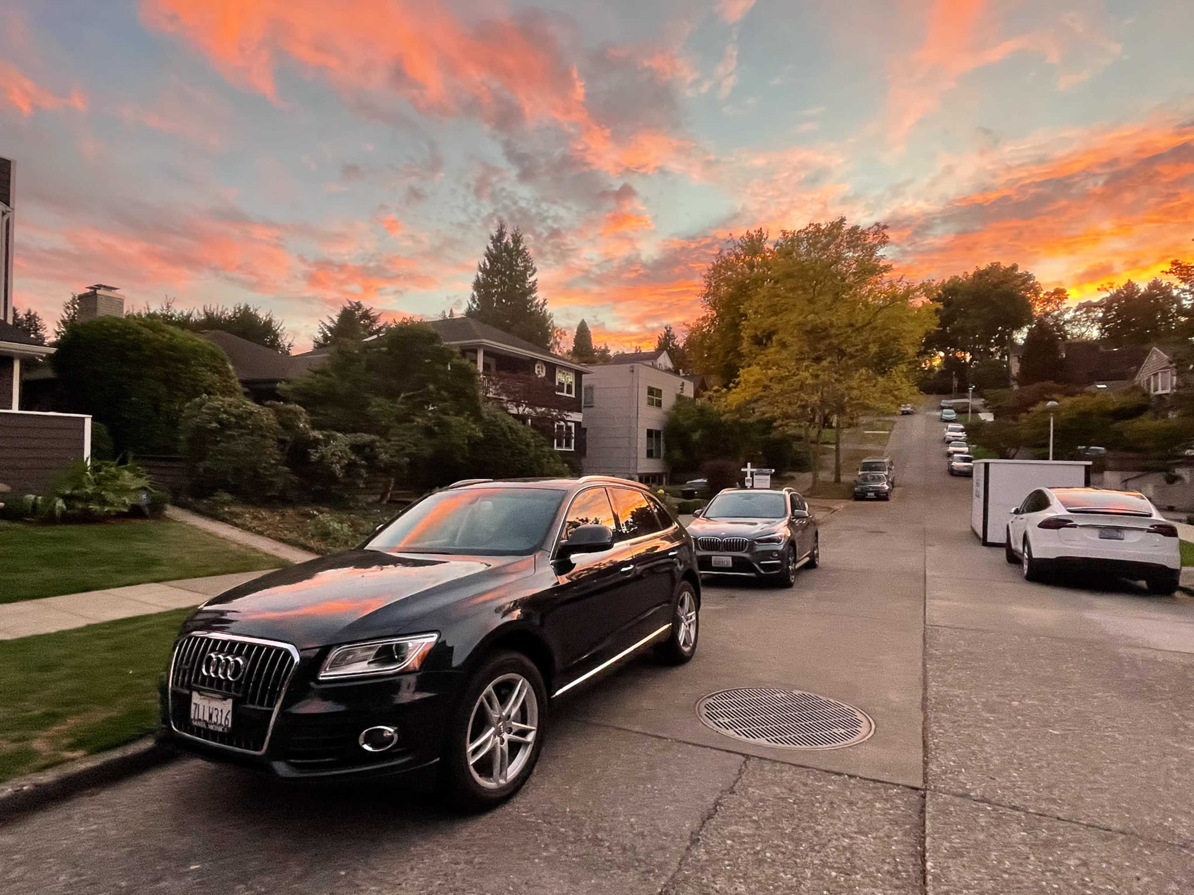 A black Audi SUV parked on a residential street with colorful clouds at sunset.