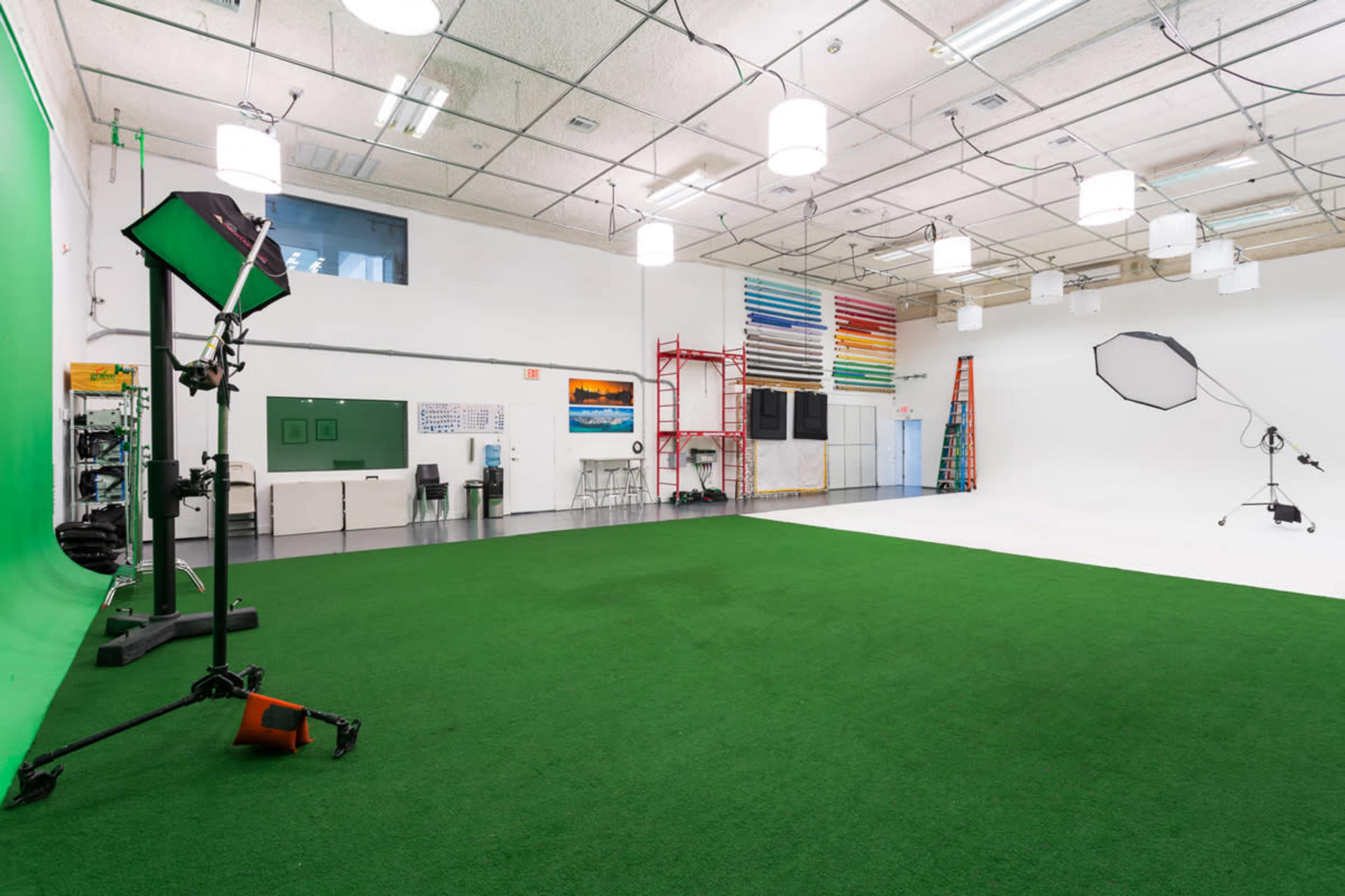 A spacious studio with a green screen, various lighting equipment, and a white backdrop, all set against a carpet of artificial grass.