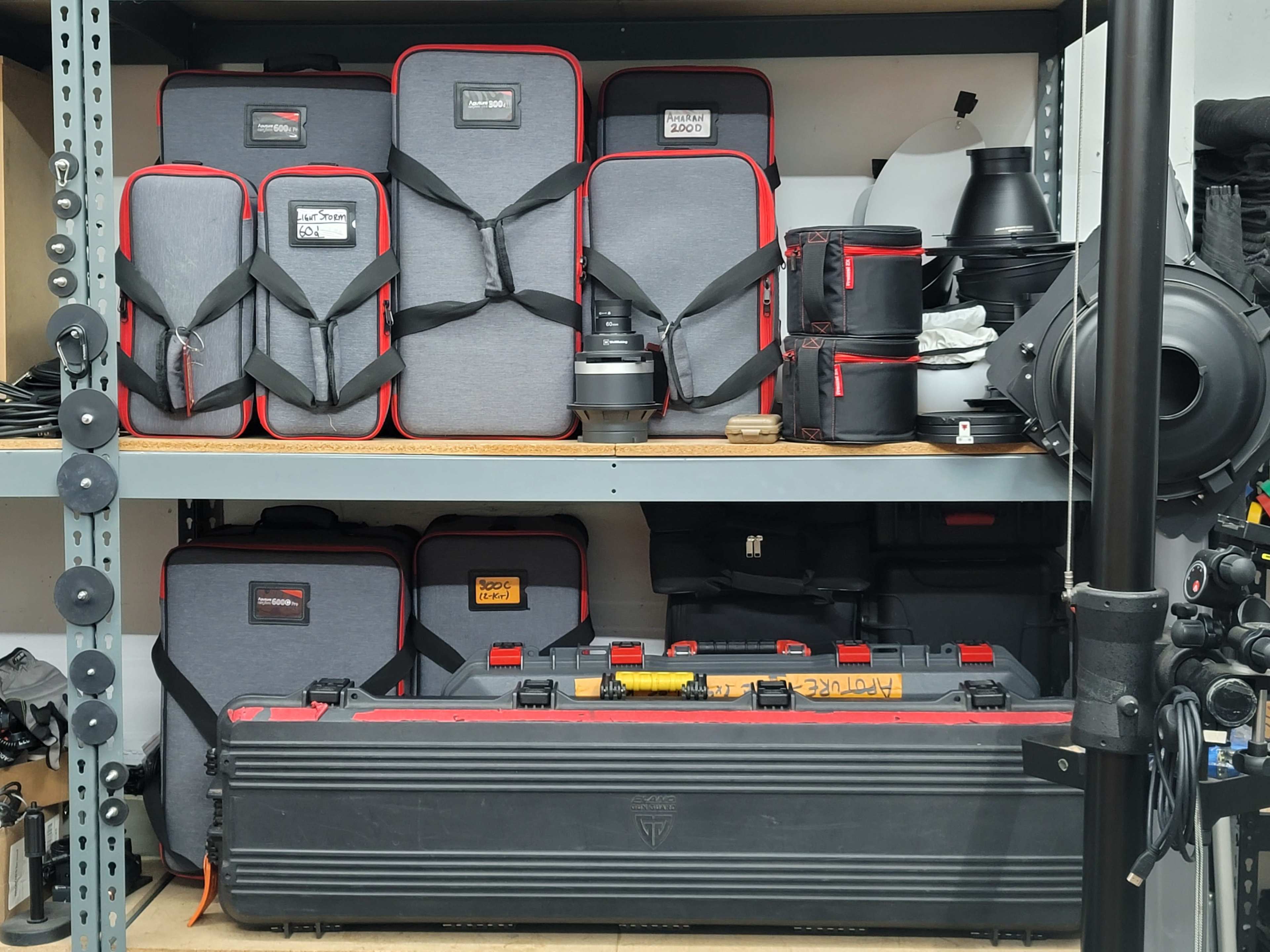 A set of neatly organized camera equipment cases and accessories are arranged on a shelf in a storage area.