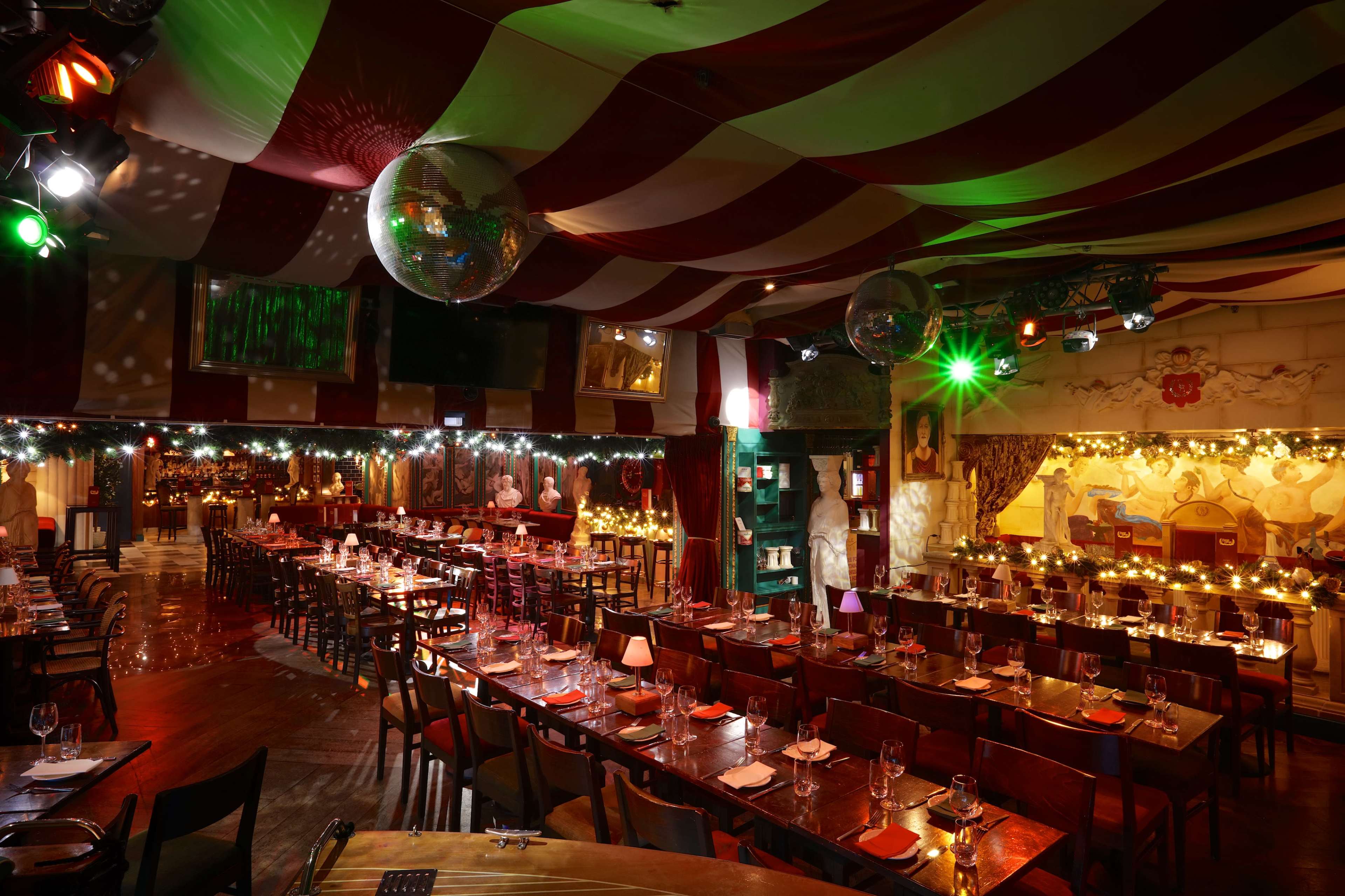 A restaurant interior with red and white striped fabric draping overhead, tables set with silverware, and disco balls hanging from the ceiling.