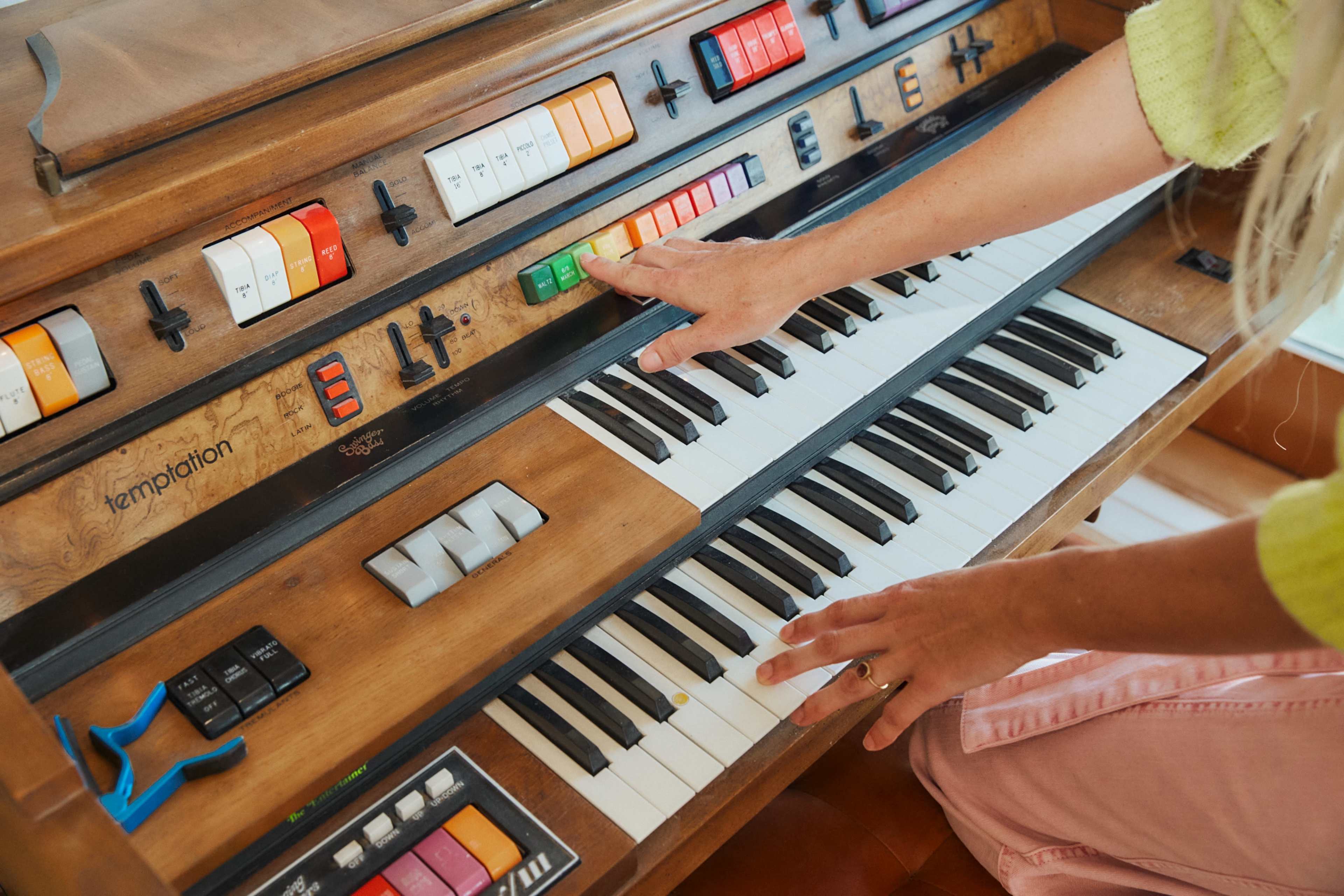 A person’s hand is pressing a green key on a vintage organ with colorful buttons and a black and white keyboard.