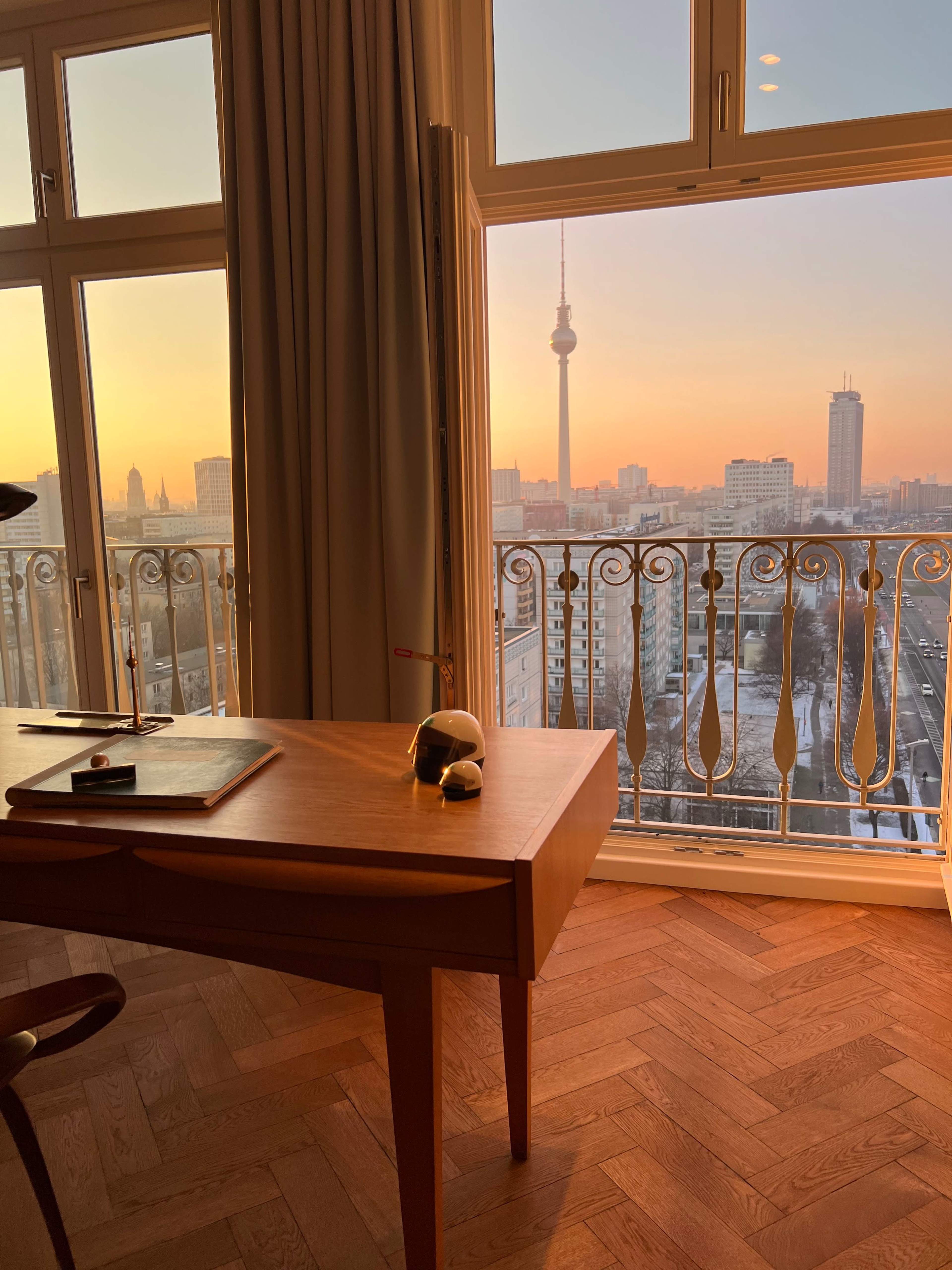A modern workspace with a desk and a scenic view of the Berlin skyline at sunset, featuring the TV Tower in the distance.