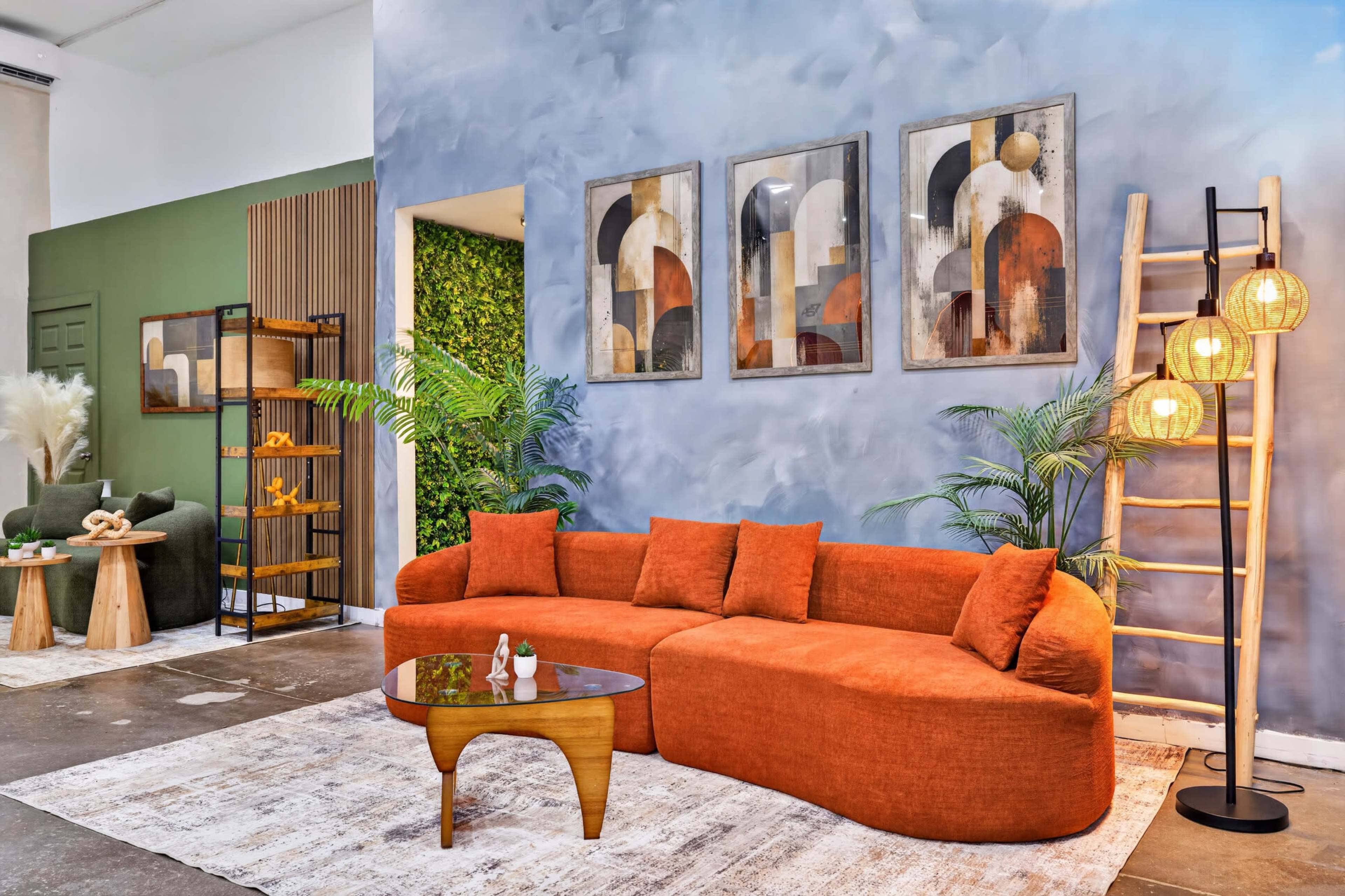The image shows a modern living room featuring an orange sectional sofa, a round coffee table, decorative wall art, and a green plant backdrop.