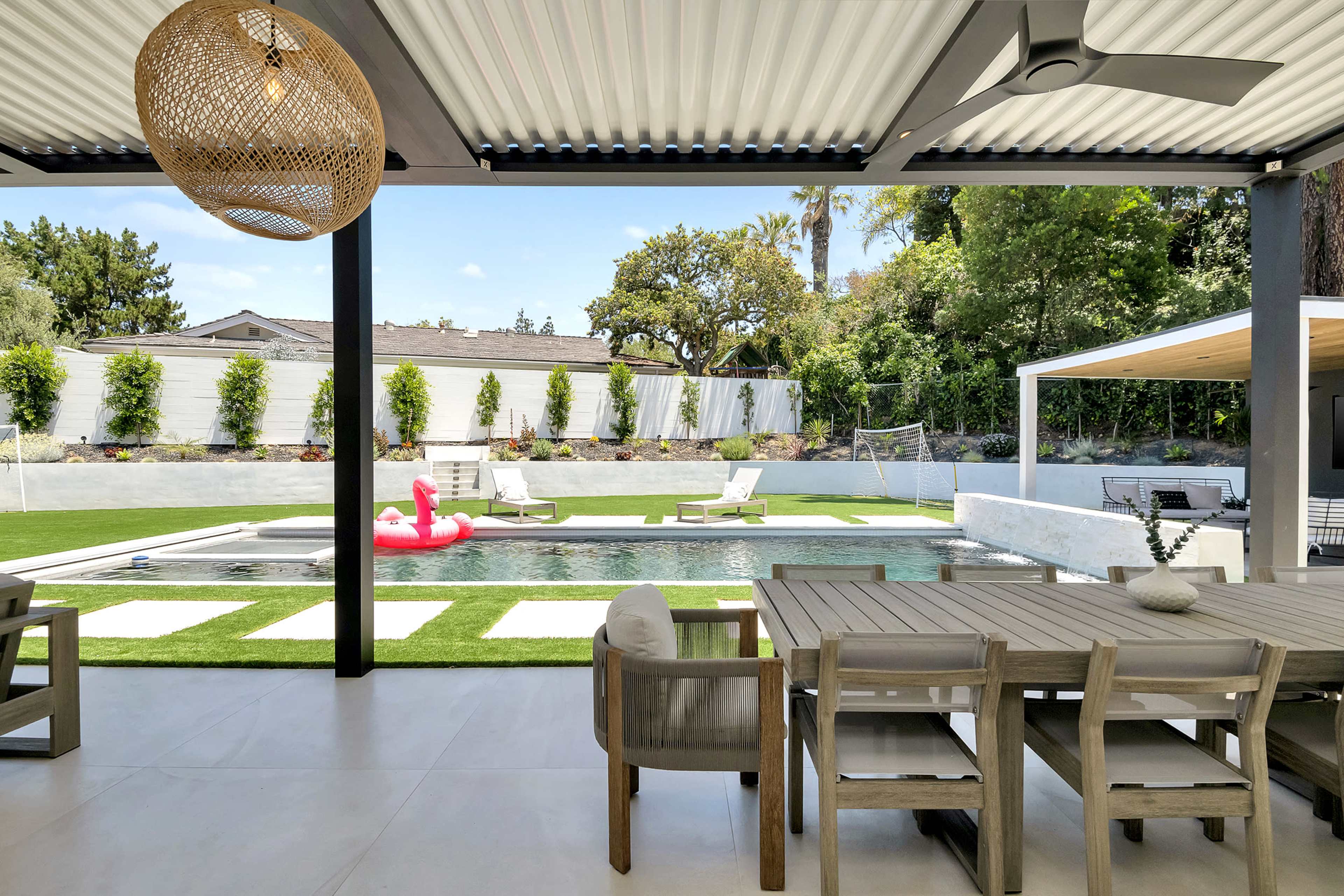 A patio area overlooking a well-maintained backyard with a pool, lounge chairs, and green landscaping.