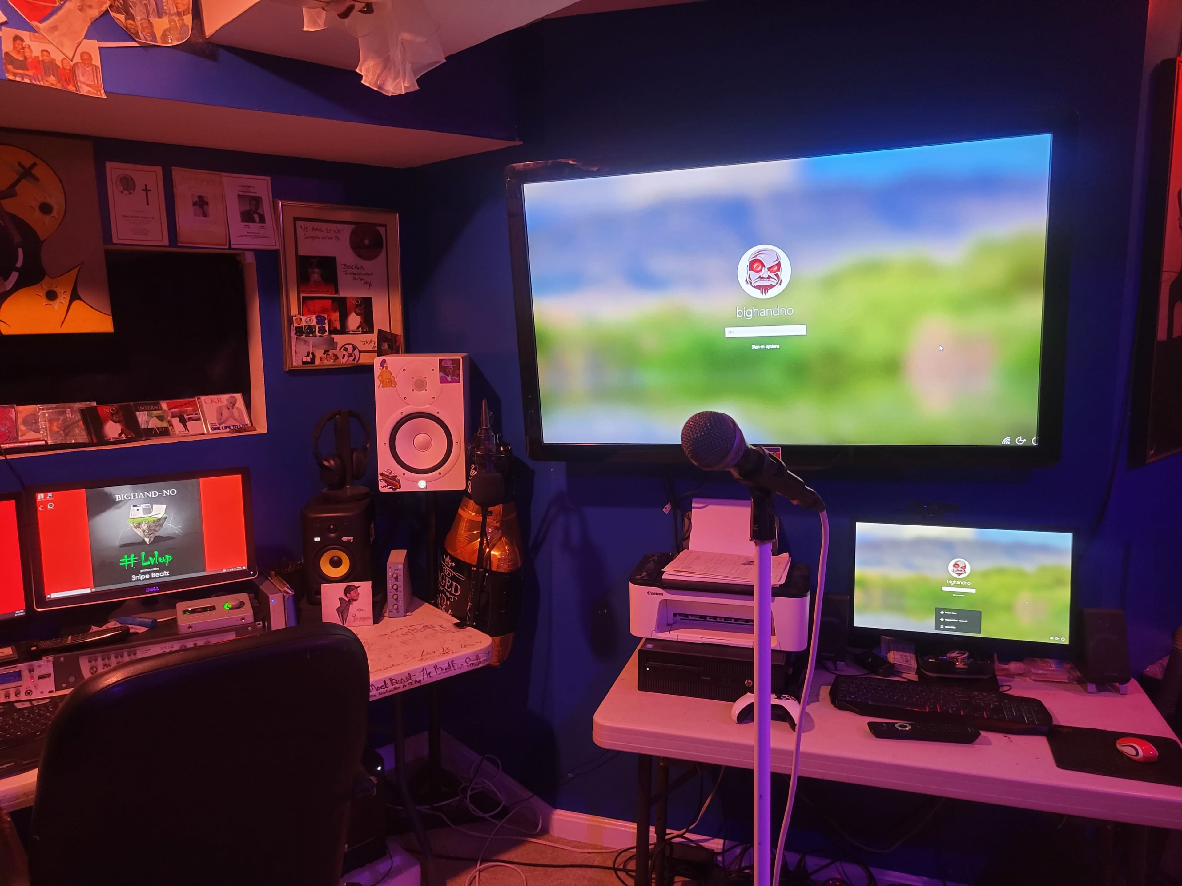 A home studio setup with multiple computers, a microphone, and audio equipment against a blue wall.