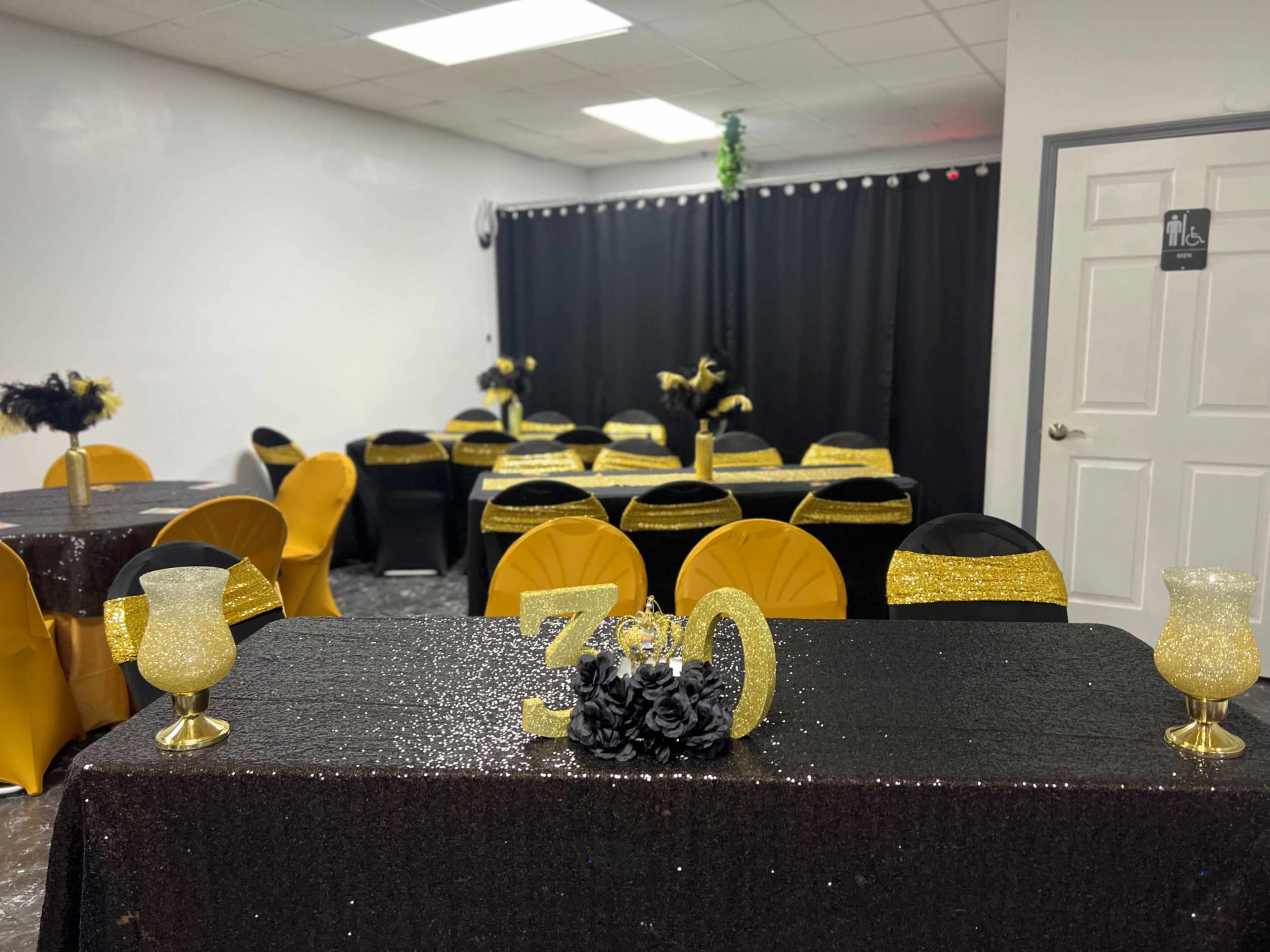 A decorated event space features tables set with black and gold tablecloths and centerpieces, with a large "30" display at the front.