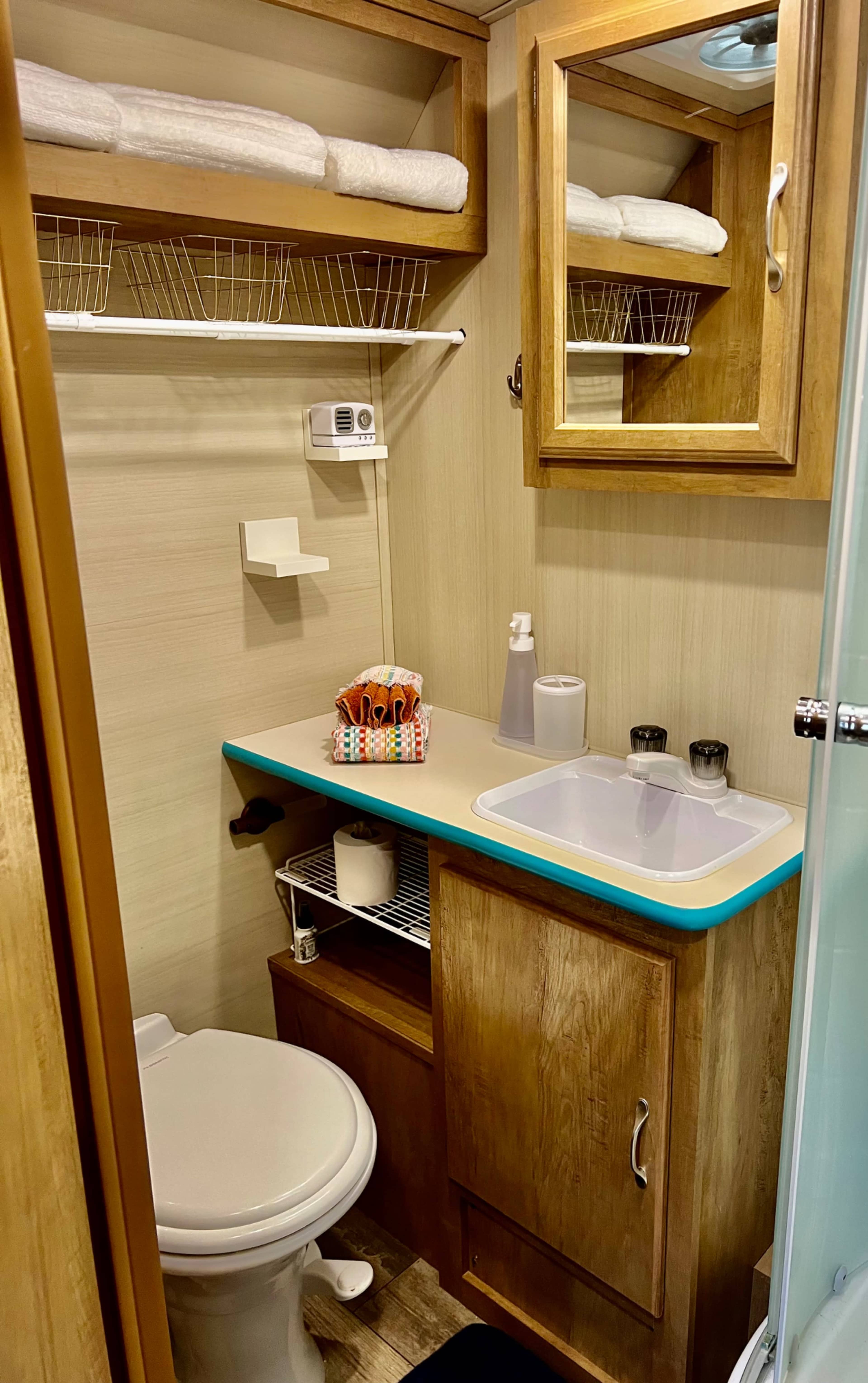 A compact bathroom featuring a toilet, a sink with a countertop, storage shelves above, and a mirror on the wall.
