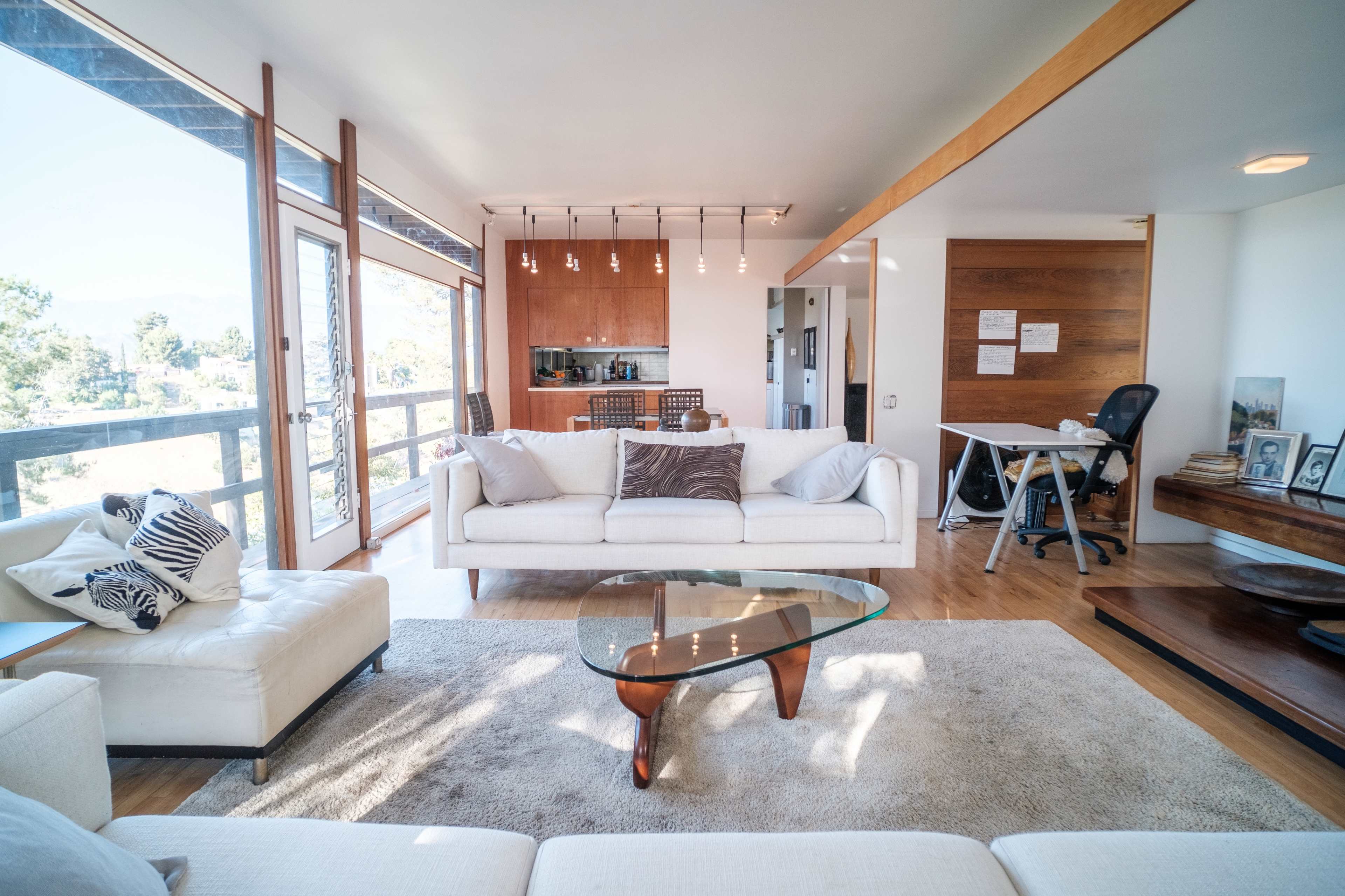 A modern living room with a white sofa, a glass coffee table, and a view of a kitchen area in the background.