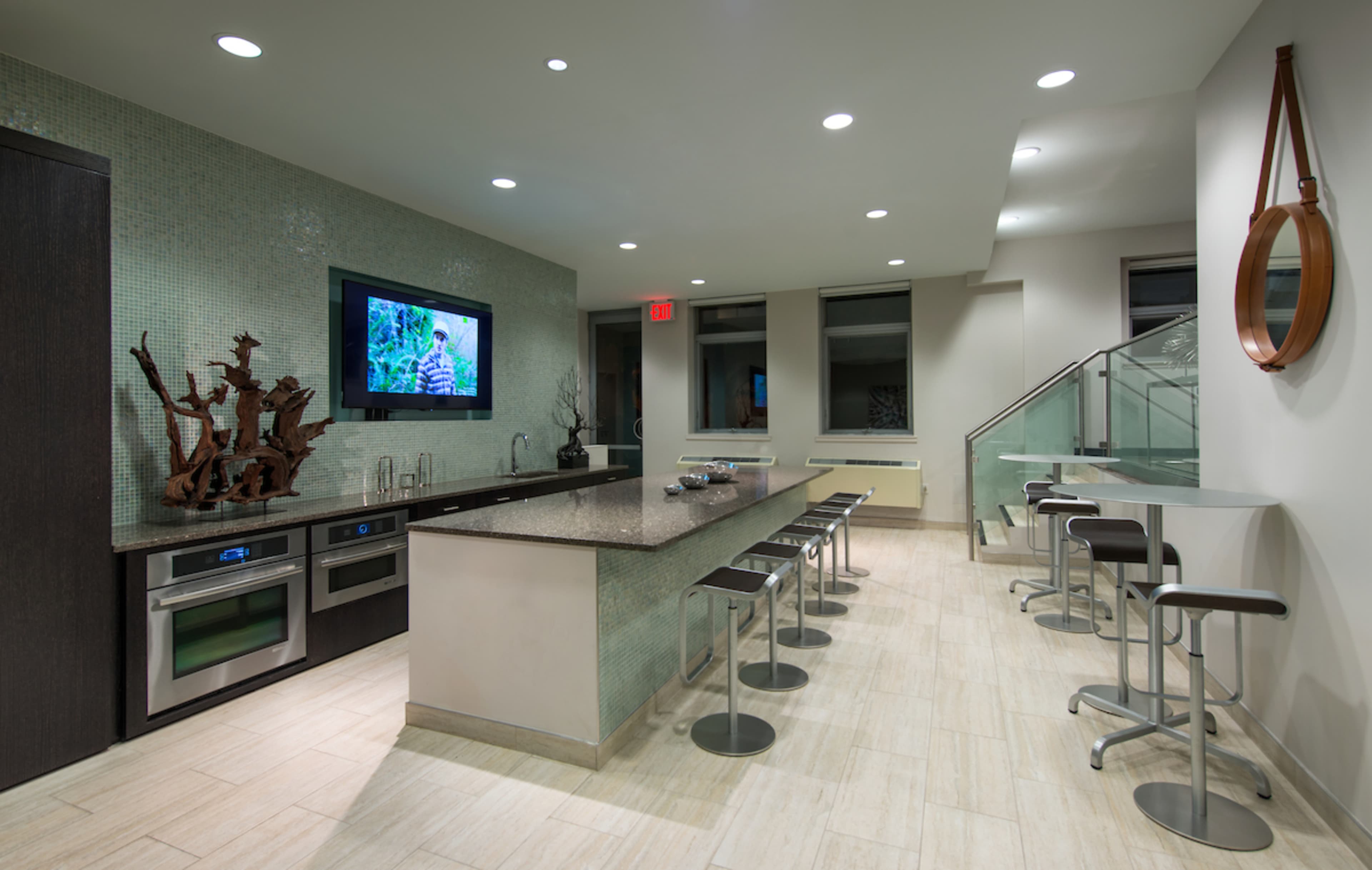 A modern kitchen features a central island with bar stools, stainless steel appliances, and a television mounted on the wall.