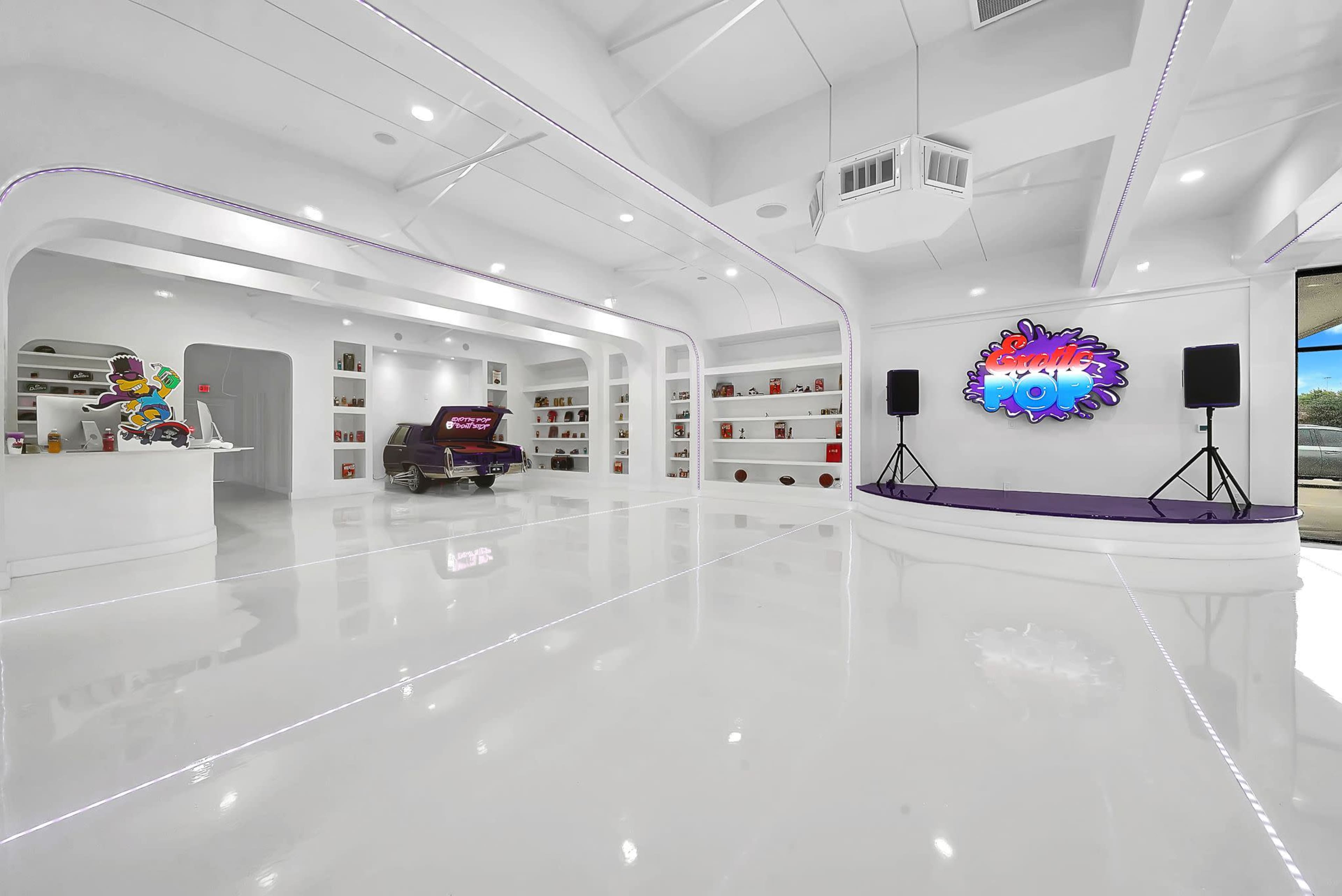 The interior features a modern, spacious gallery with white walls, glossy floors, and vibrant artwork displayed on shelves.