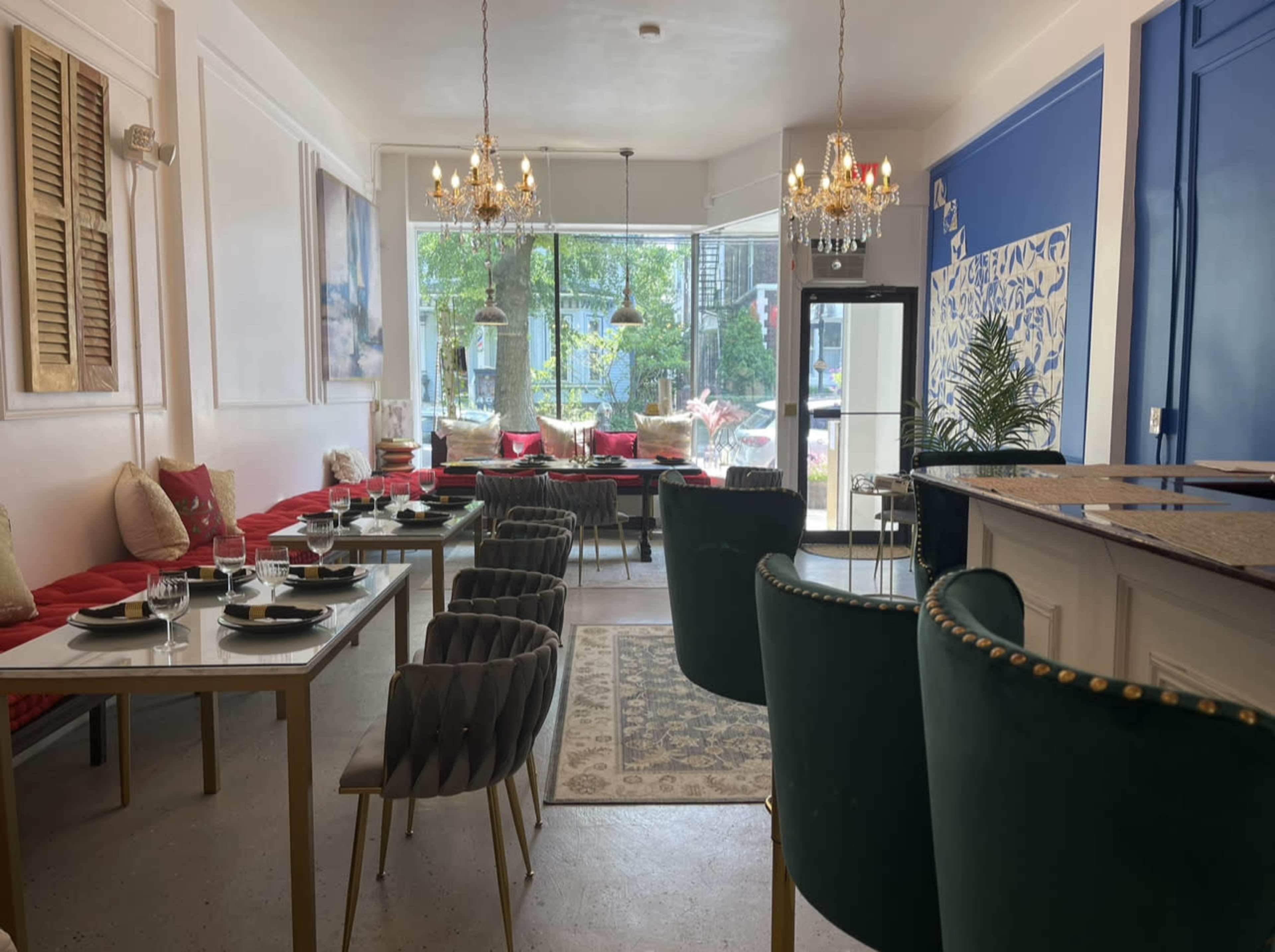 A modern restaurant interior with red seating along the walls, tables set for dining, and elegant chandeliers hanging from the ceiling.