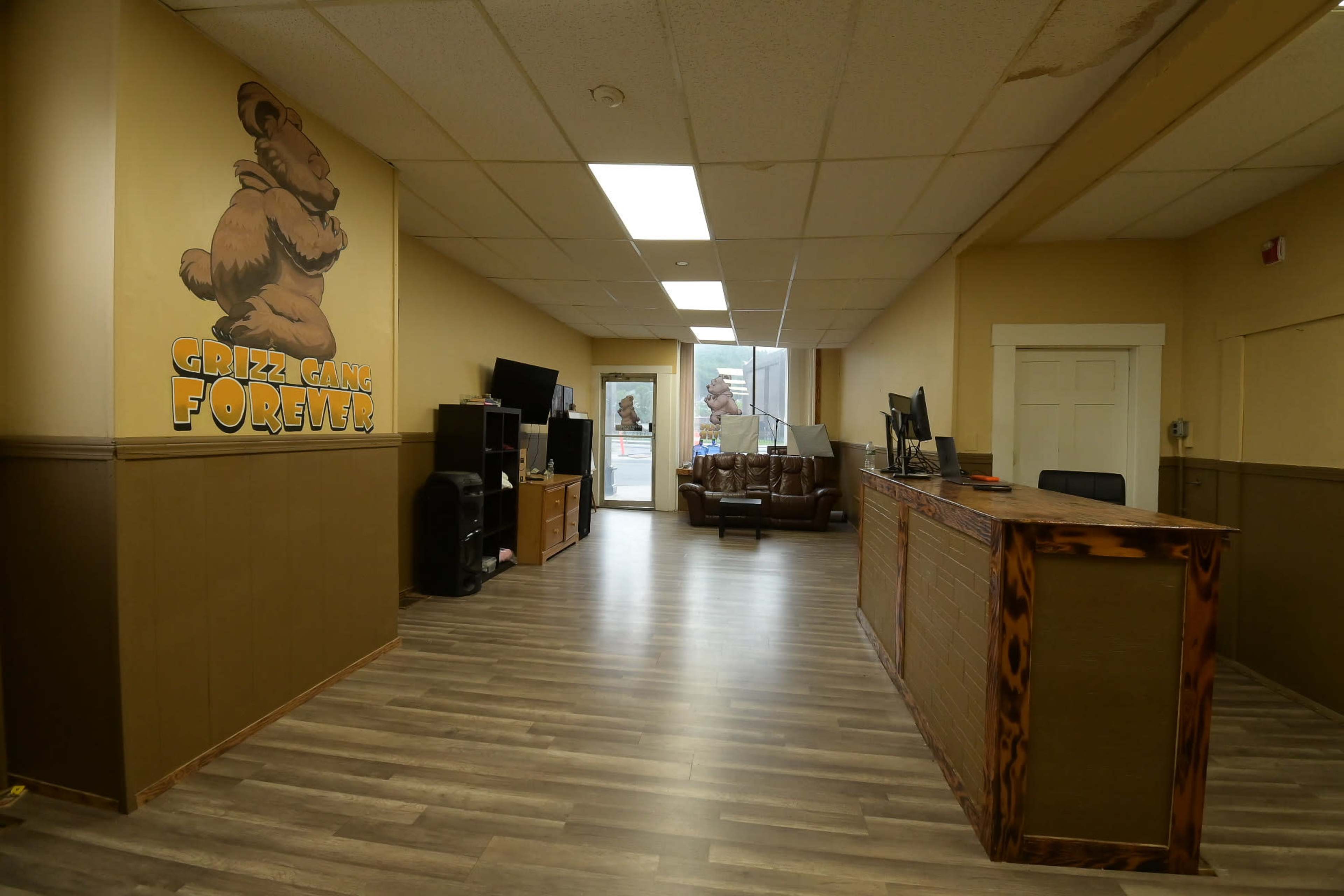 The image shows a reception area with a wooden front desk, a couch, television, and a mural of a bear on the wall.