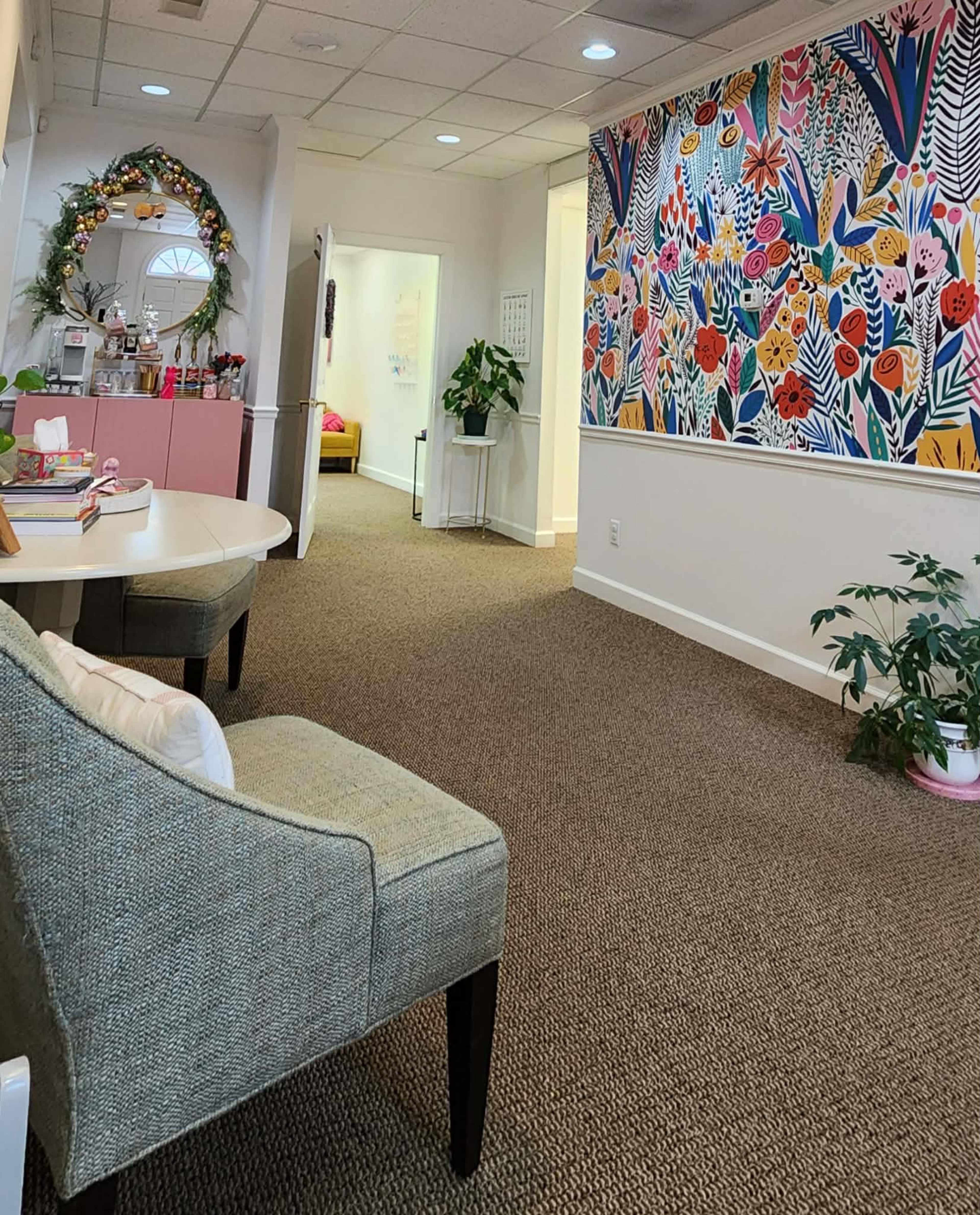 The image shows a bright waiting area with a colorful floral mural on one wall and a cozy seating arrangement featuring a gray chair.