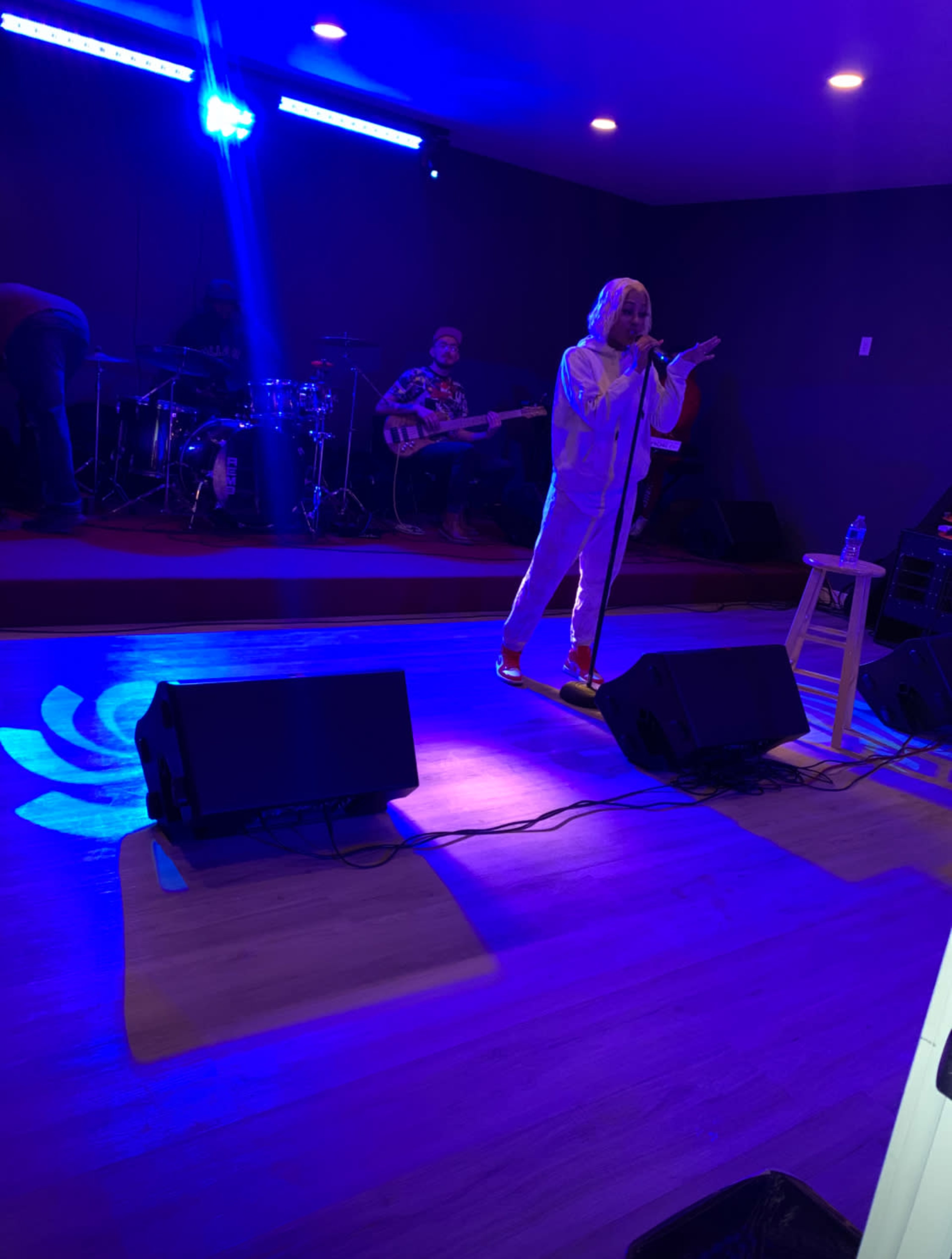 A singer performs on stage in front of a band while blue lights illuminate the setting.