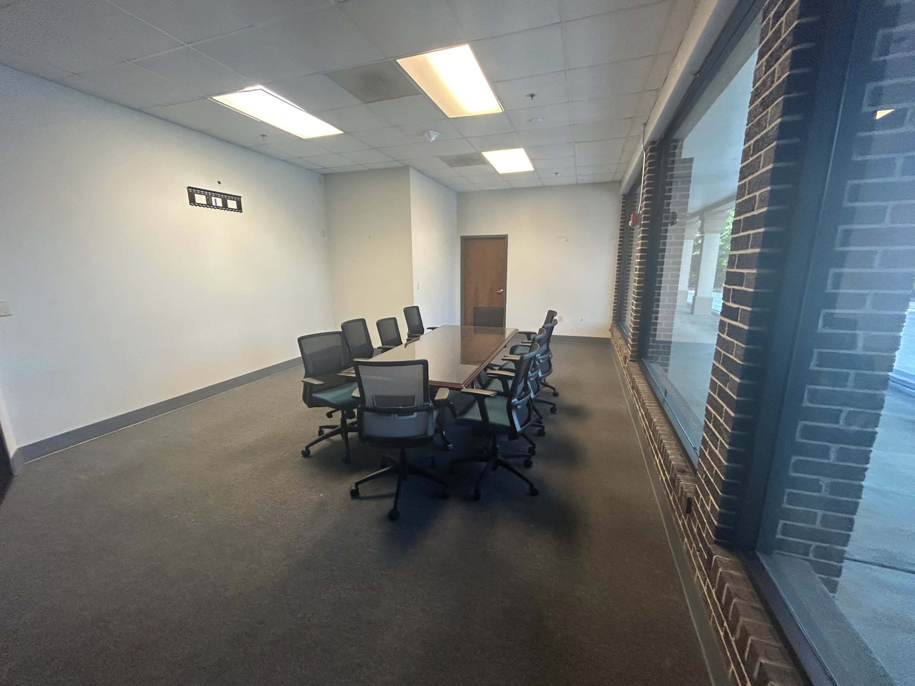 A rectangular conference room features a table surrounded by chairs, with a large window and a door on one side.