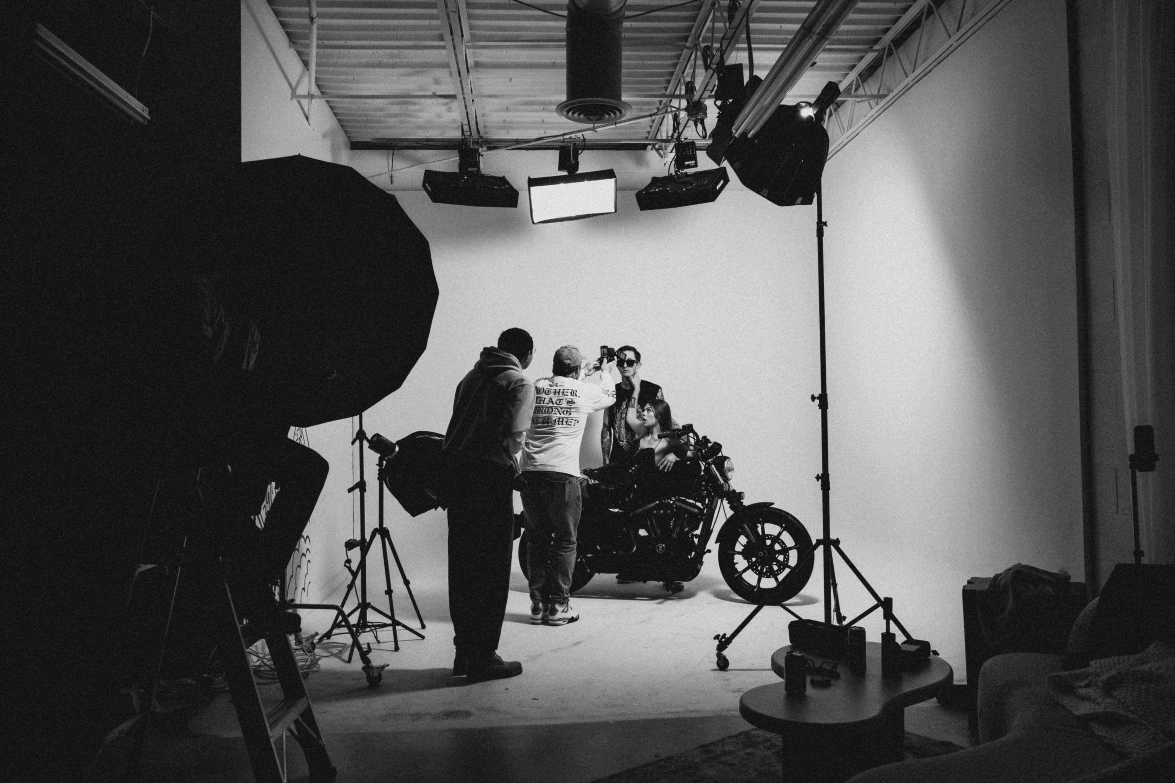 A motorcycle is positioned in a photography studio where several individuals are setting up equipment and preparing for a shoot.