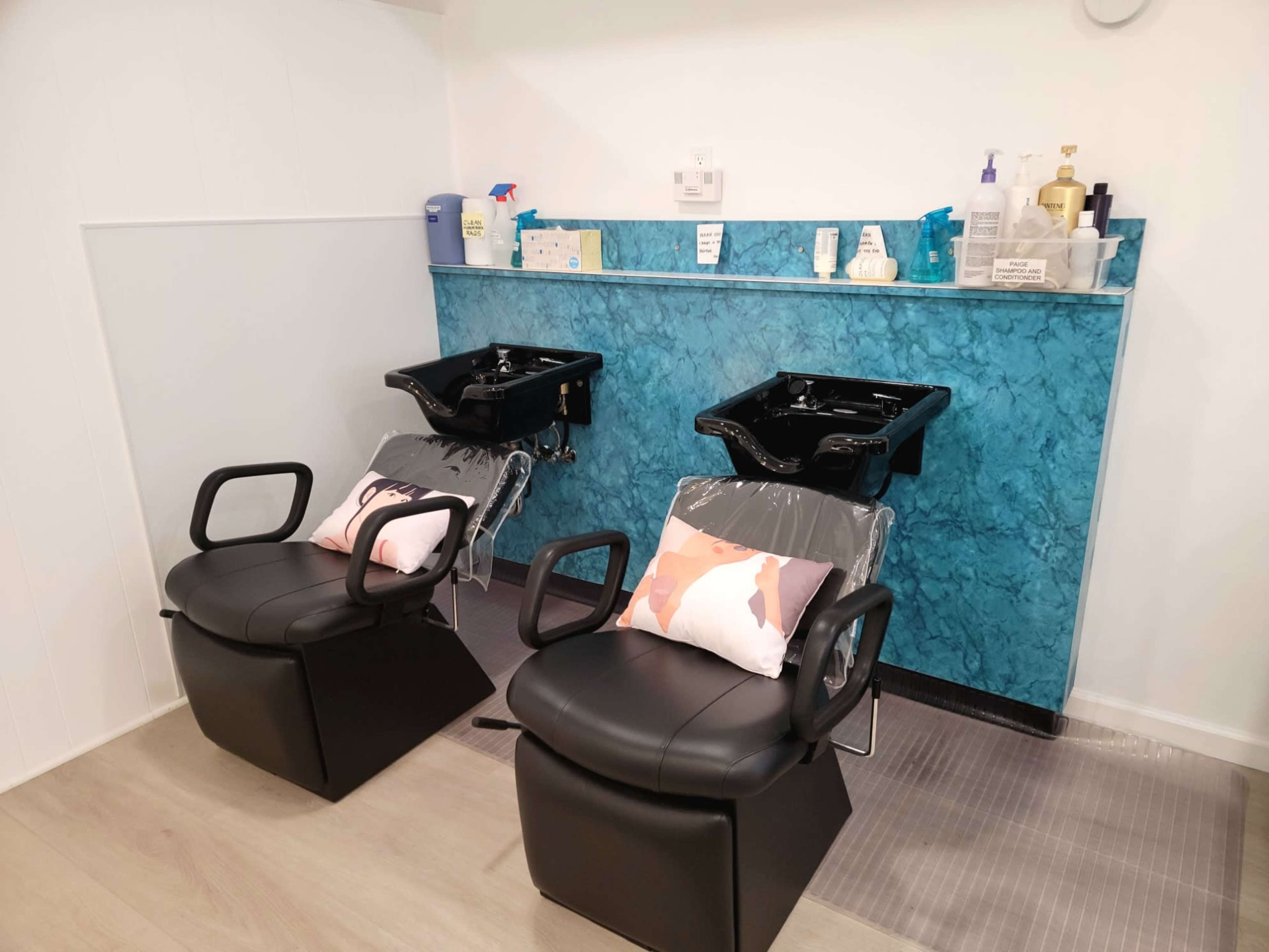 Two black salon chairs with sink basins set against a blue marble wall in a hair salon.