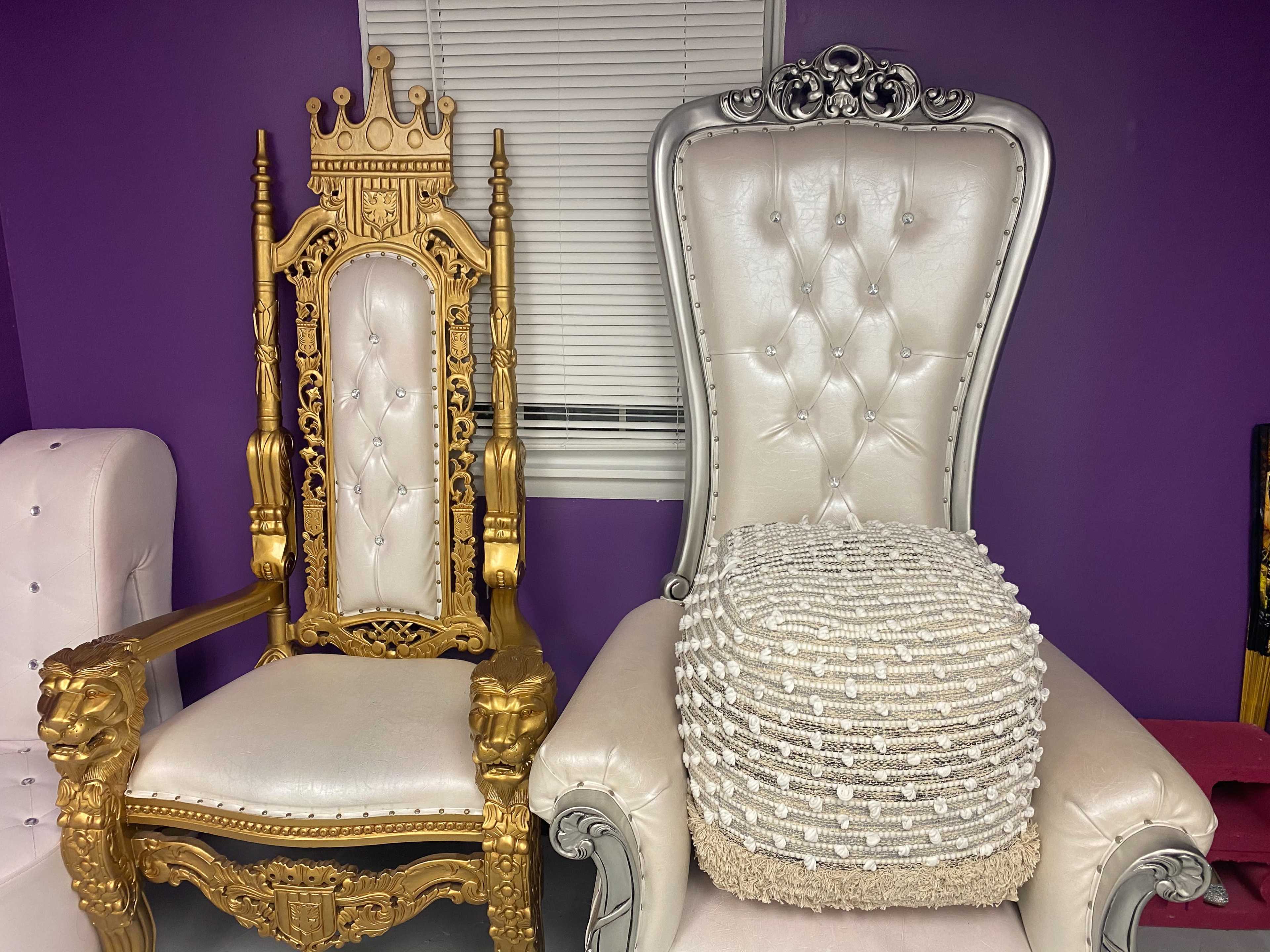 Two ornate chairs side by side: a gold throne with a crown design on the back and a plush silver chair with tufted upholstery.