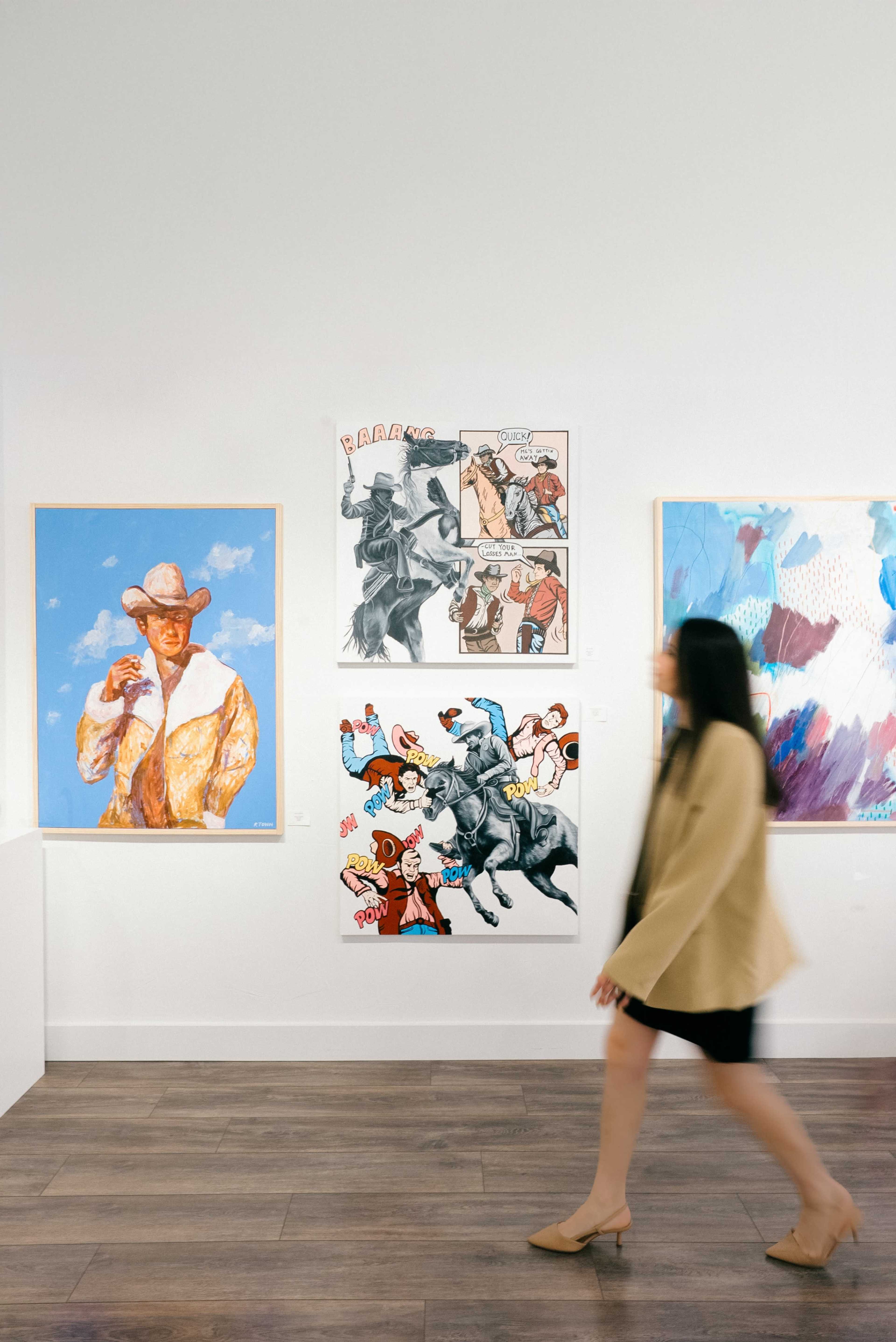 A person walks past a gallery wall displaying various pieces of artwork in a museum setting.